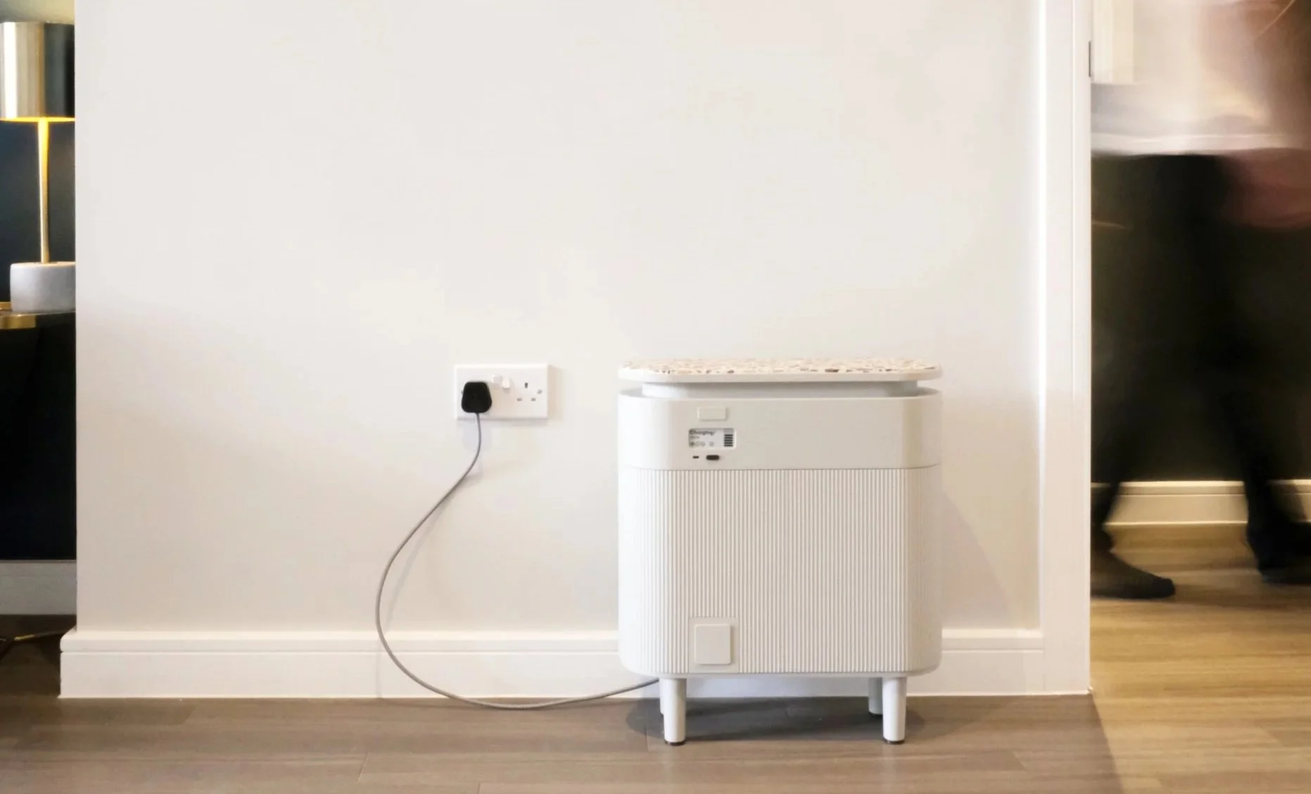 Windfall plug-in battery plugged into a plain white wall as a flat tenant walks past in the background.