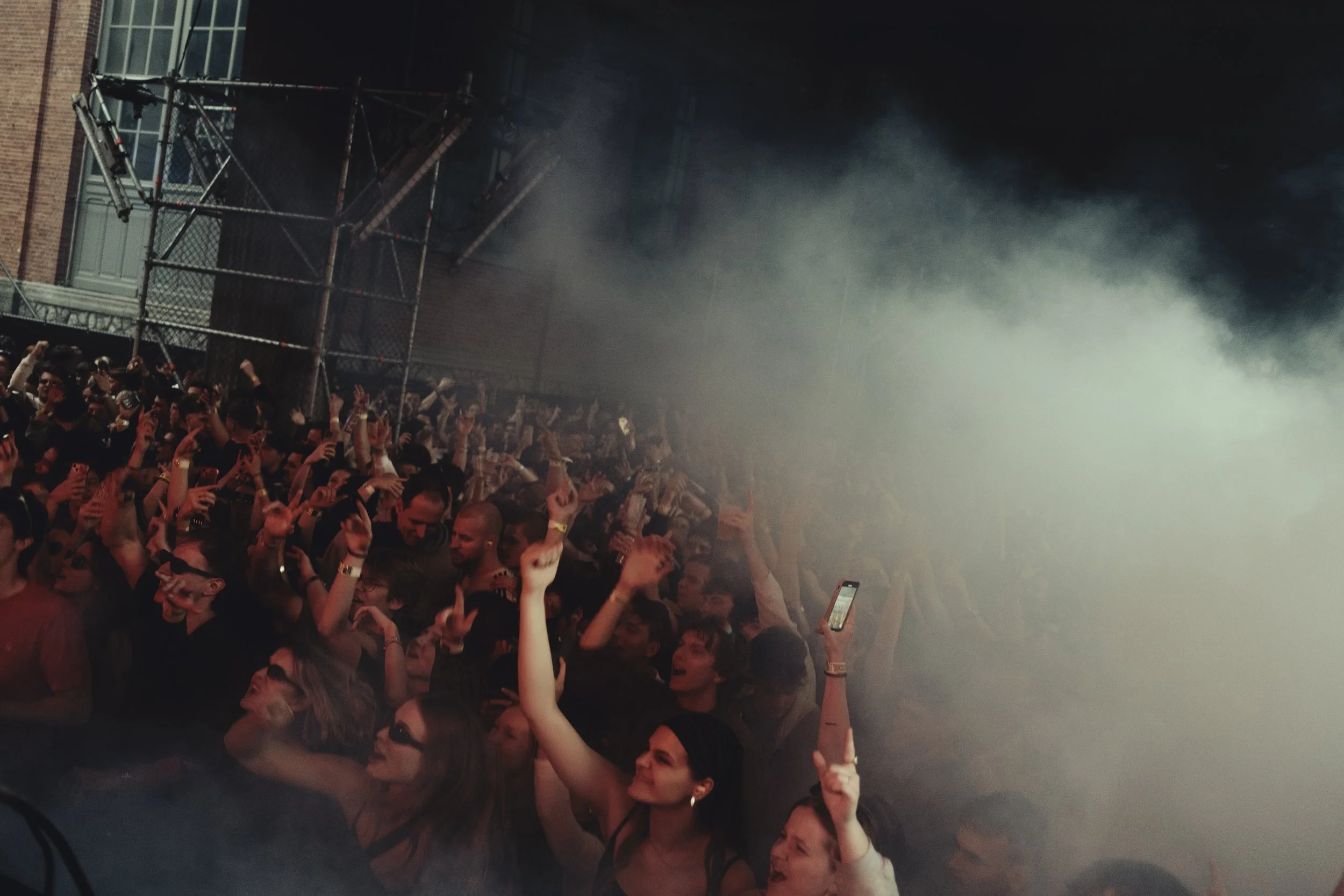 Publiek op een concert of feest met mensen die dansen en genieten, omgeven door rook of mist.