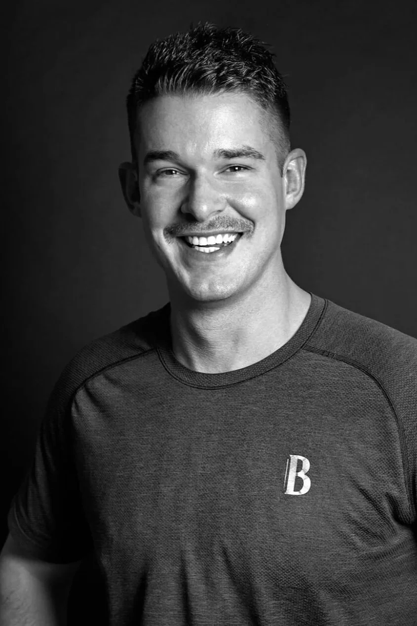 Black and white portrait of a smiling man with a moustache, short hair, and wearing a casual shirt.