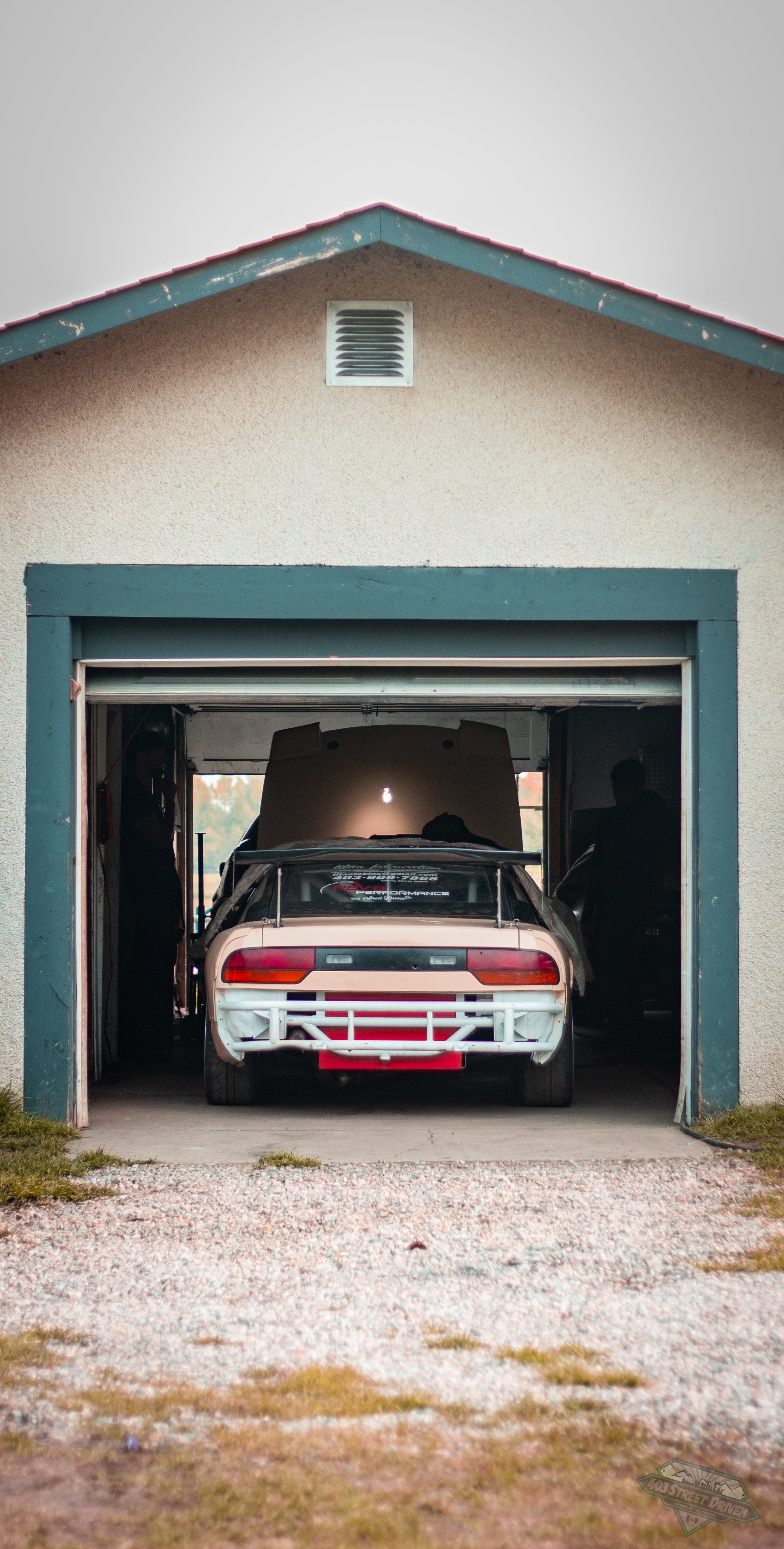 A vintage race car inside a garage with an open door, with a person standing to the right.