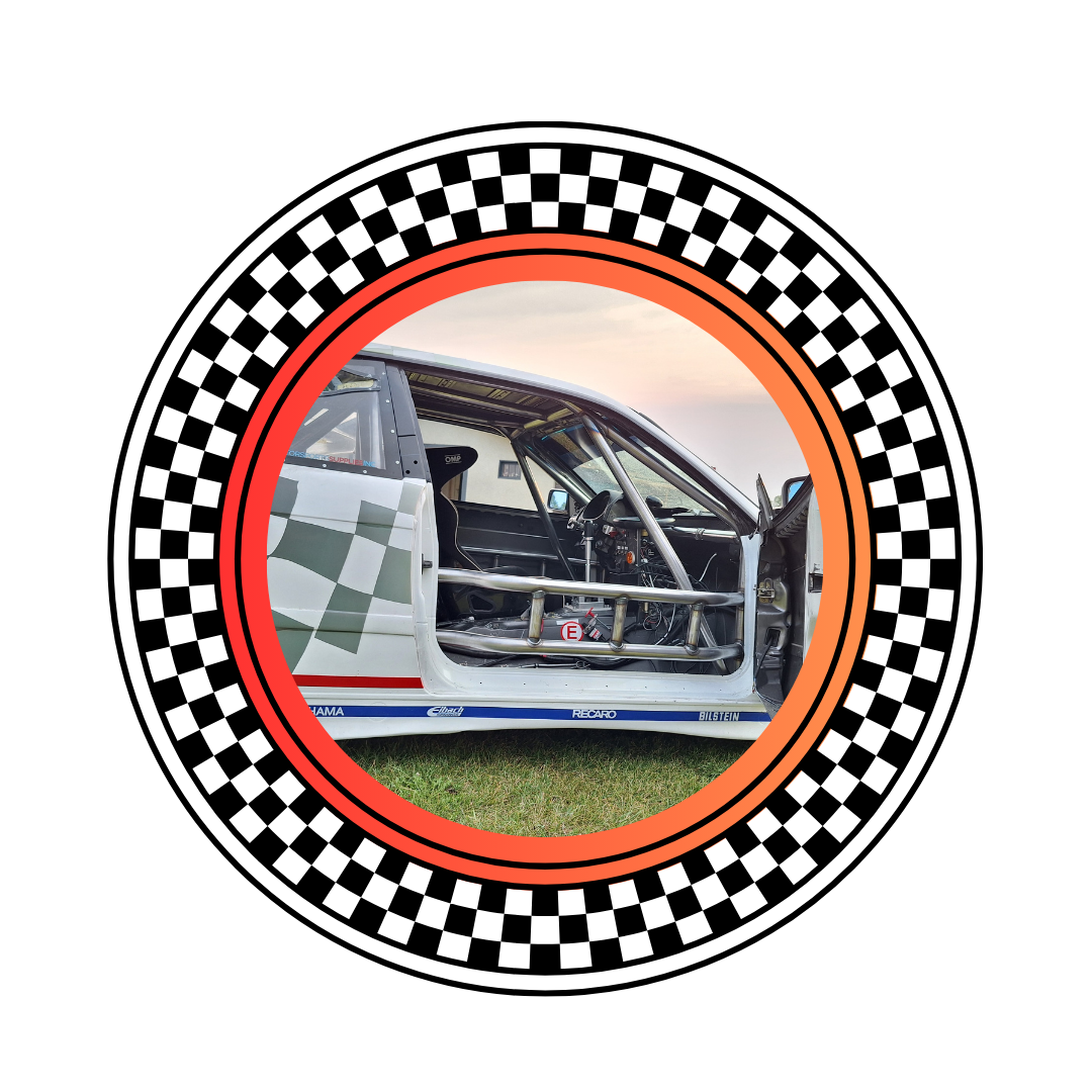 Race car interior with roll cage, racing seat, and dashboard, photographed outdoors during sunset.