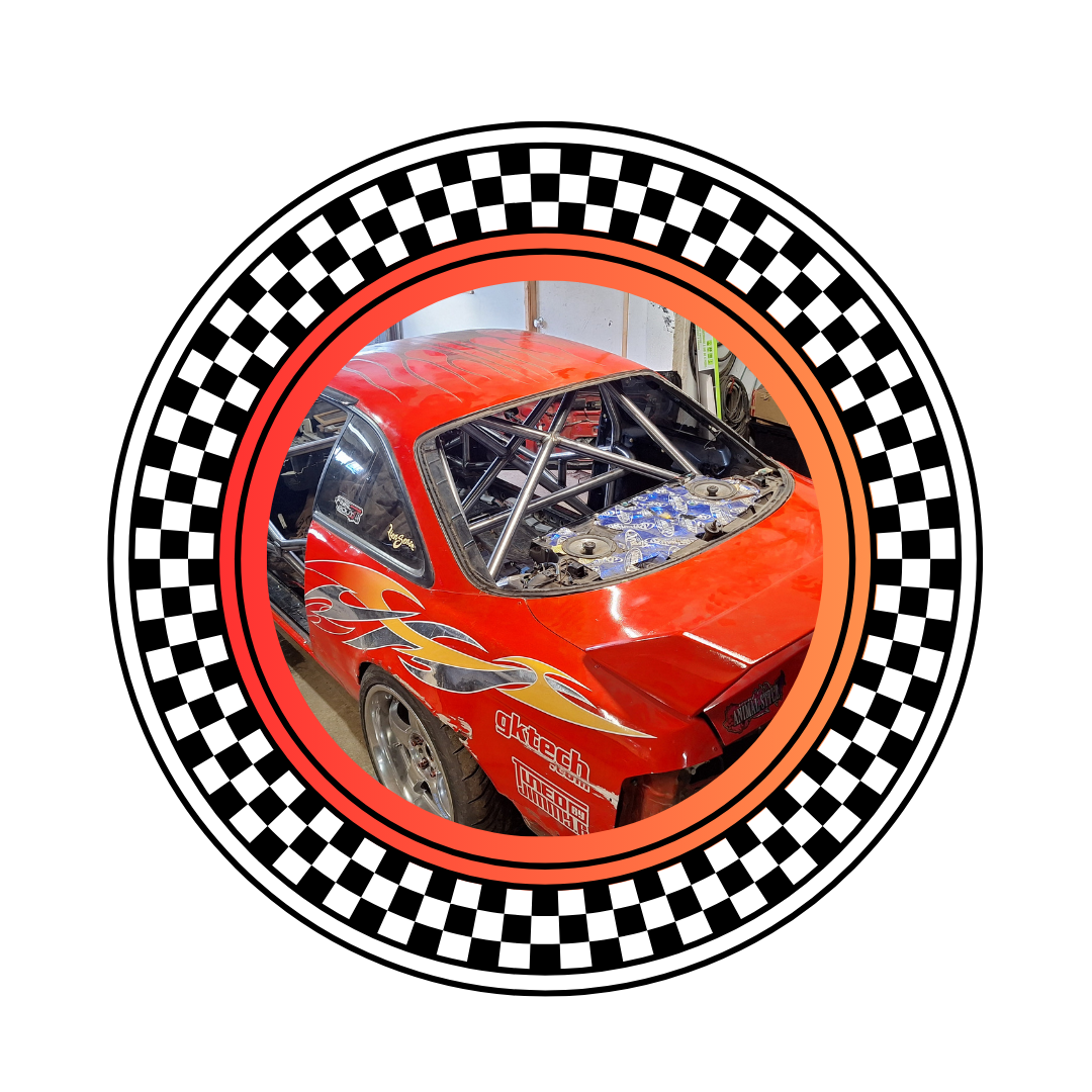 Inside a racing car with a red body and flame decals, showing an exposed engine bay and a custom roll cage, surrounded by racing flags.