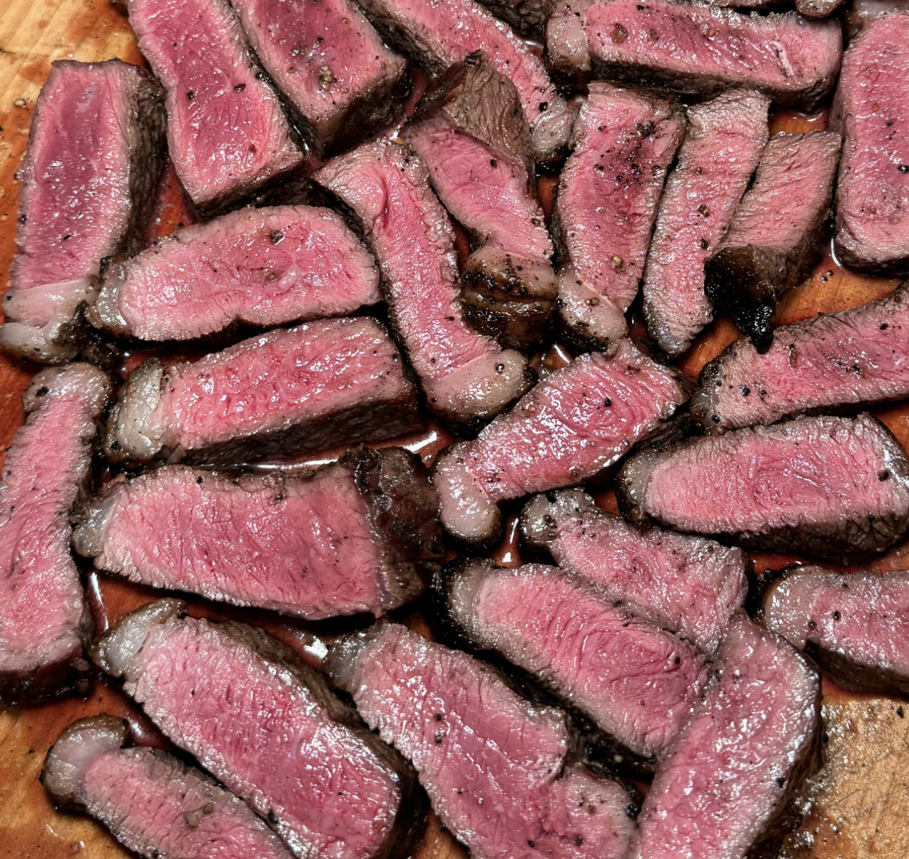 Slices of cooked steak with a pink center on a wooden cutting board.
