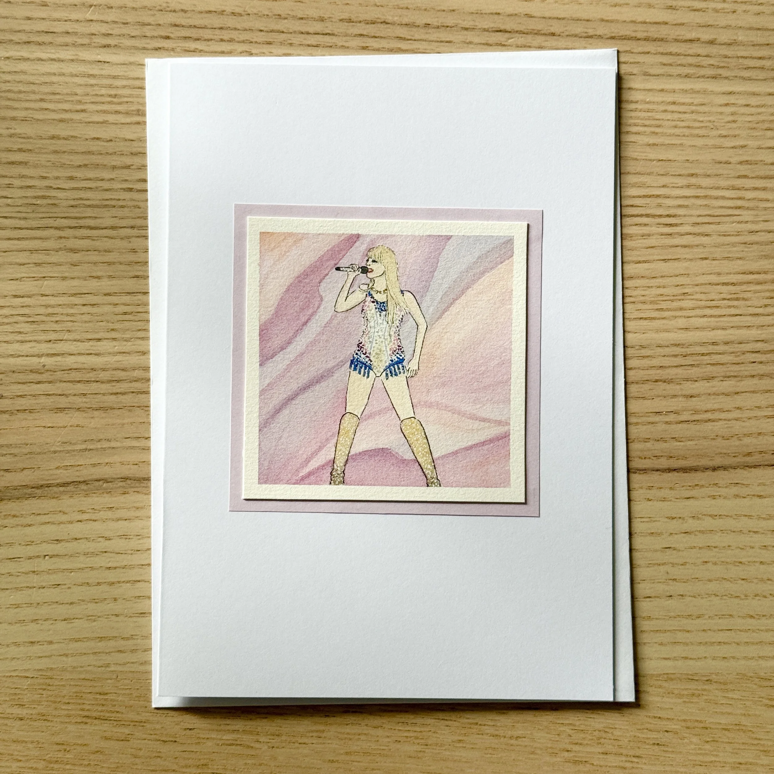 A handmade watercolour greeting card featuring a hand-painted illustration of Taylor Swift in her Lover era.