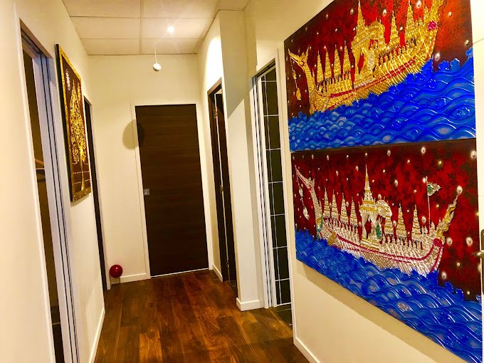 Interior hallway with wooden floor, brown door, decorative Thai-style wall art with golden boats on a blue and red background.