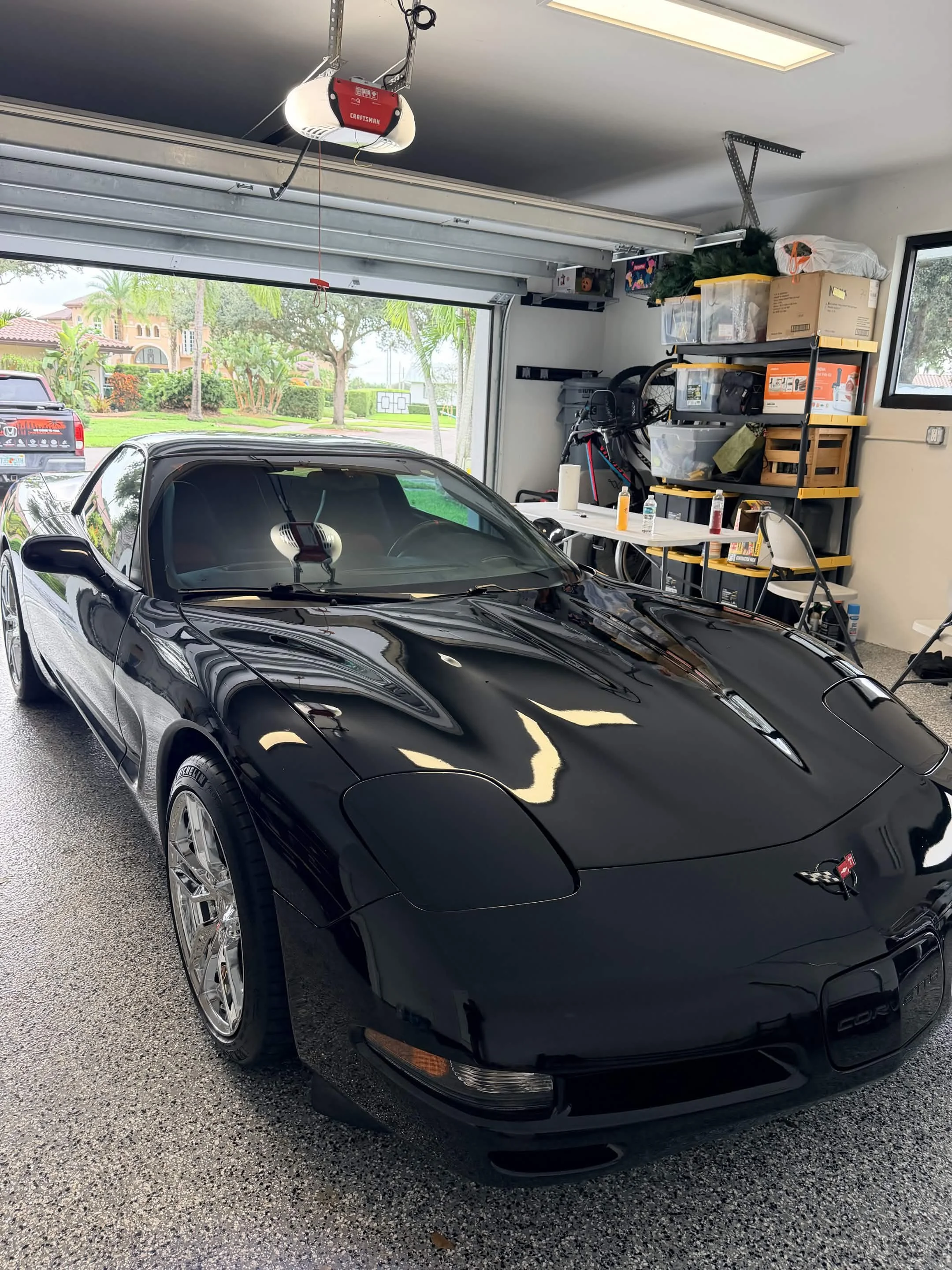Black Chevrolet Corvette sports car parked inside a garage with storage shelves in the background
