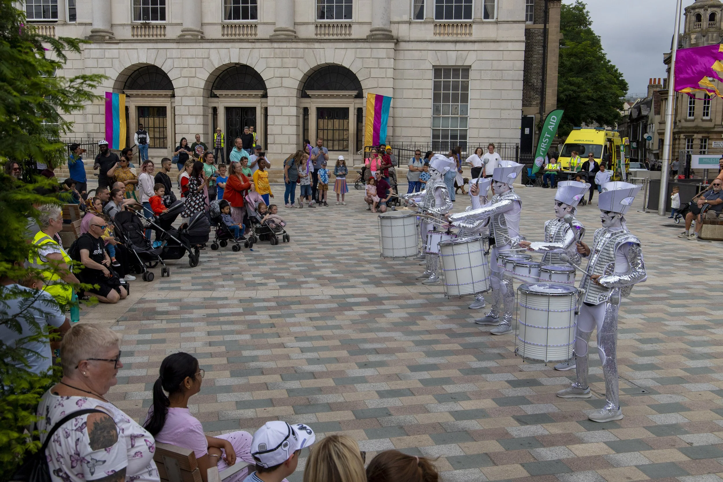 A crowd watches as drummers all dressed in white perform on a public square