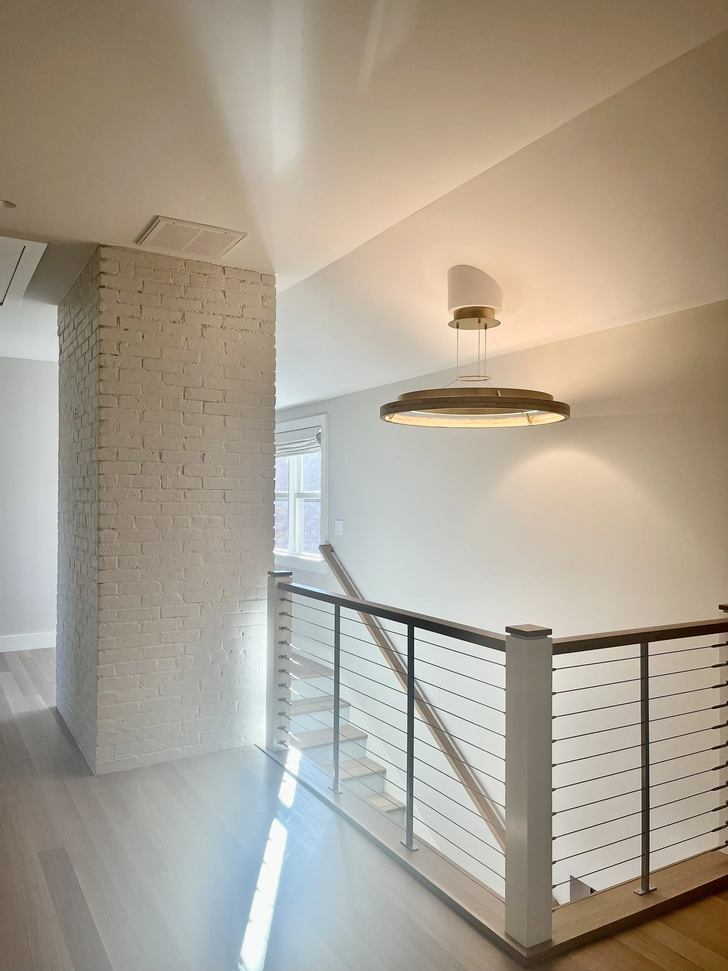 Interior of a modern home with a staircase, white walls, a hanging light fixture, and a brick pillar.
