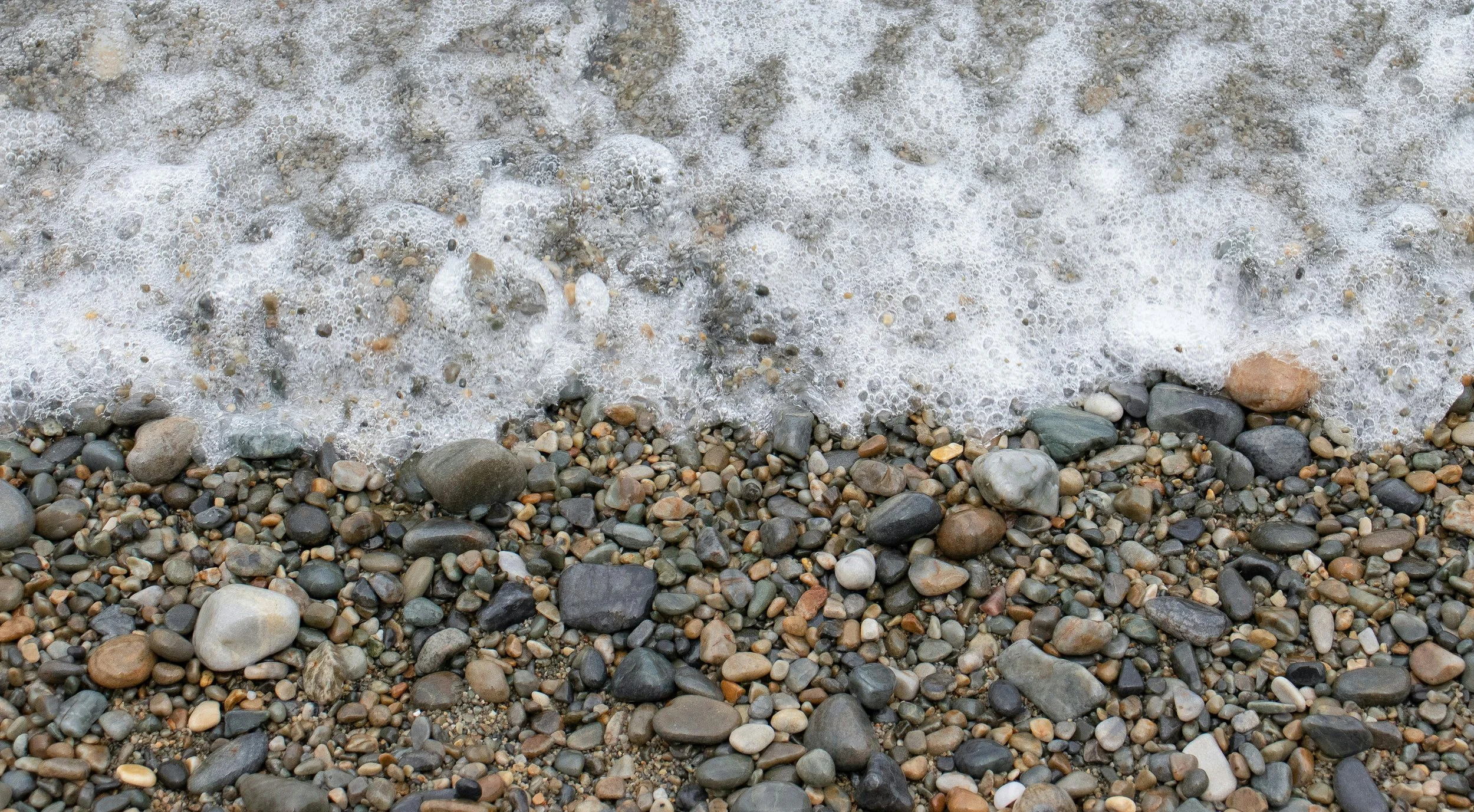 Pebbled beach with small stones and rocks as waves wash over.