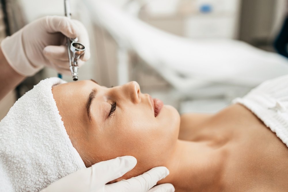 A woman receiving a facial treatment with a cosmetic device in a spa or clinic setting.