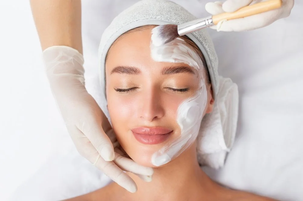 Woman receiving a facial treatment with cream applied to her face by a professional in a spa setting.