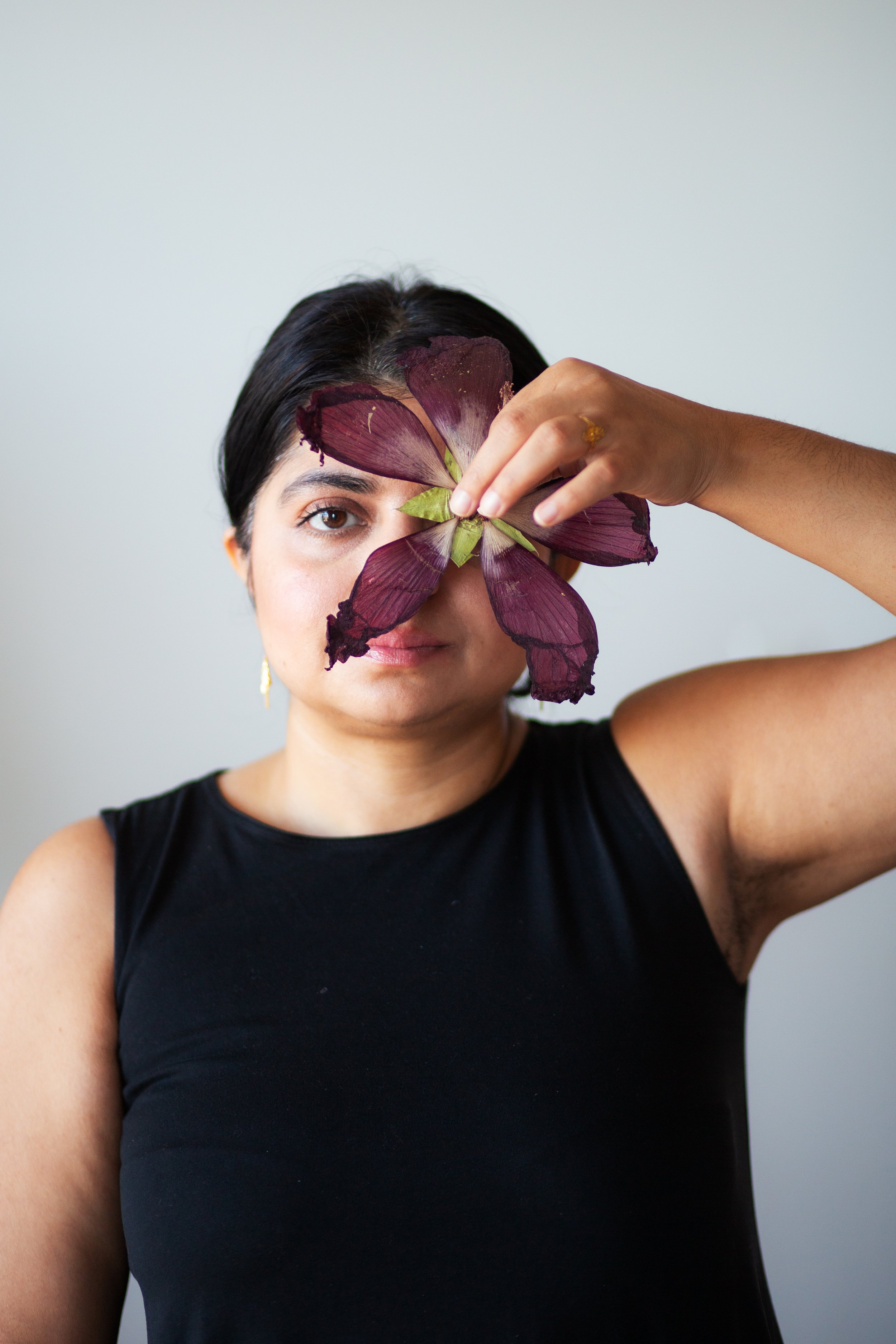 A woman holding a large purple leaf in front of her face, partially covering her right eye, against a plain gray background.