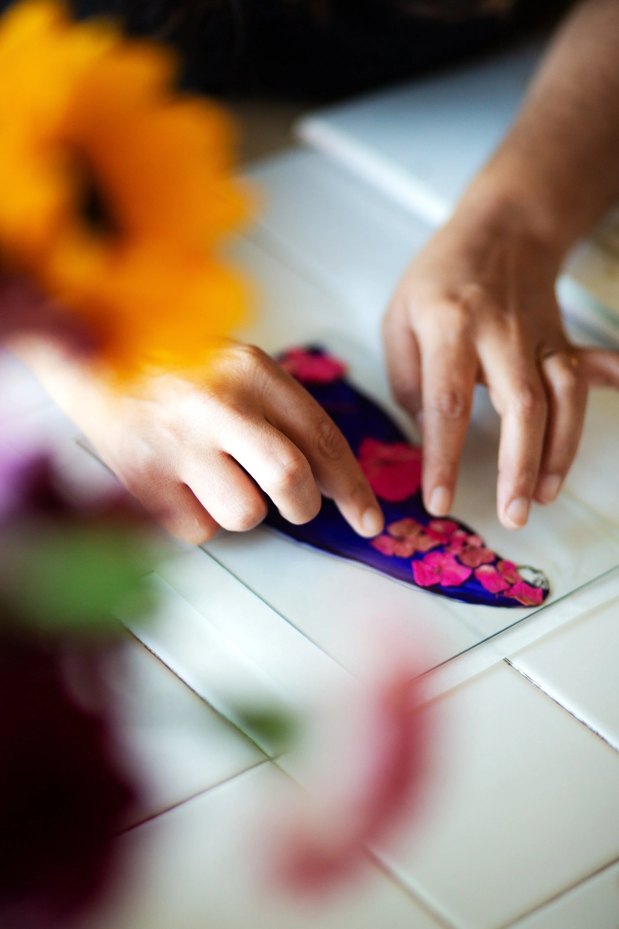 Close-up of hands placing a colorful butterfly-shaped ornament with pink flower patterns on a white tiled surface.