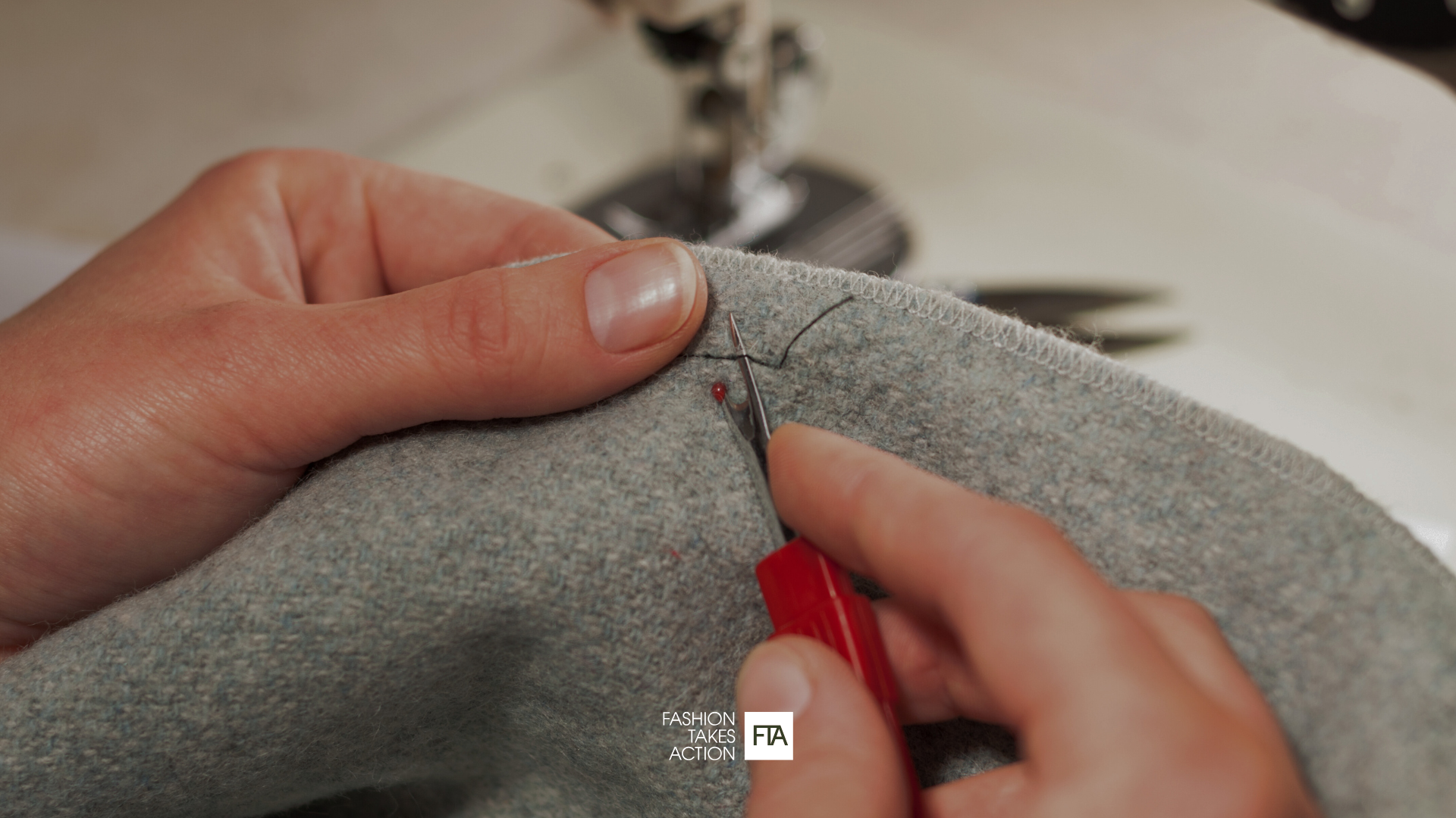 Close-up image of hands repairing a grey piece of clothing. FTA logo.