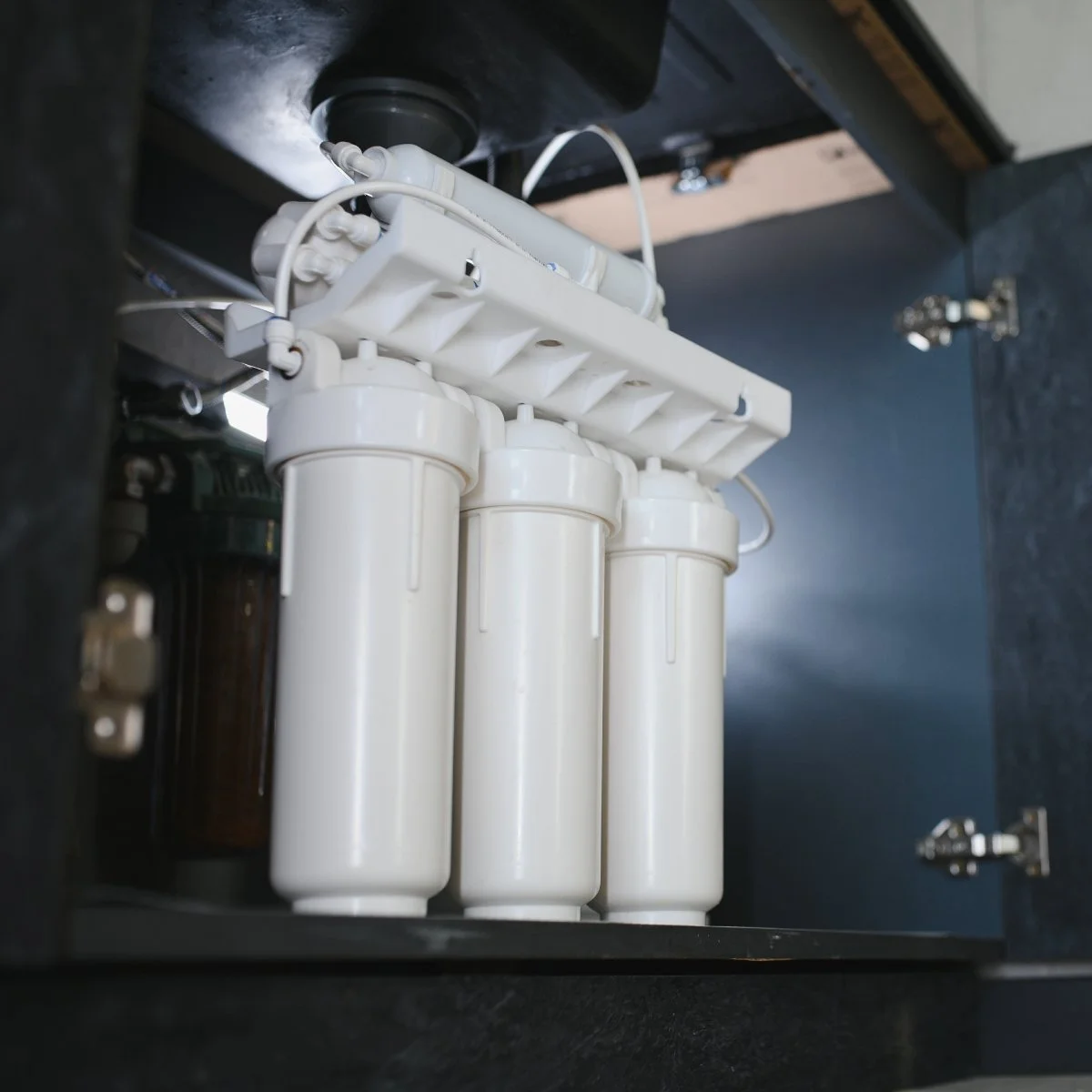 Under-sink water filtration system with white filter cartridges.
