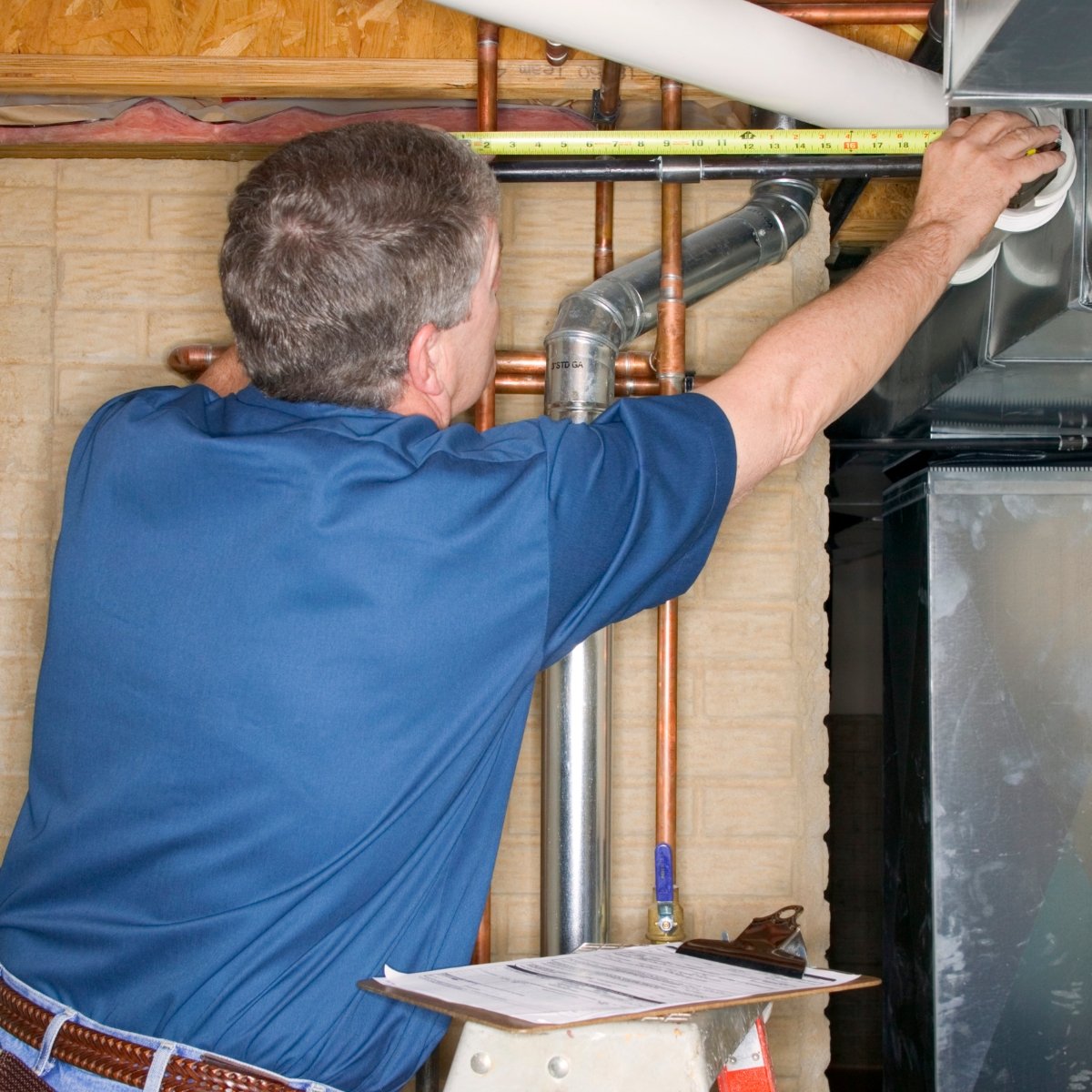 A technician working on HVAC ductwork and copper pipes in a building."}