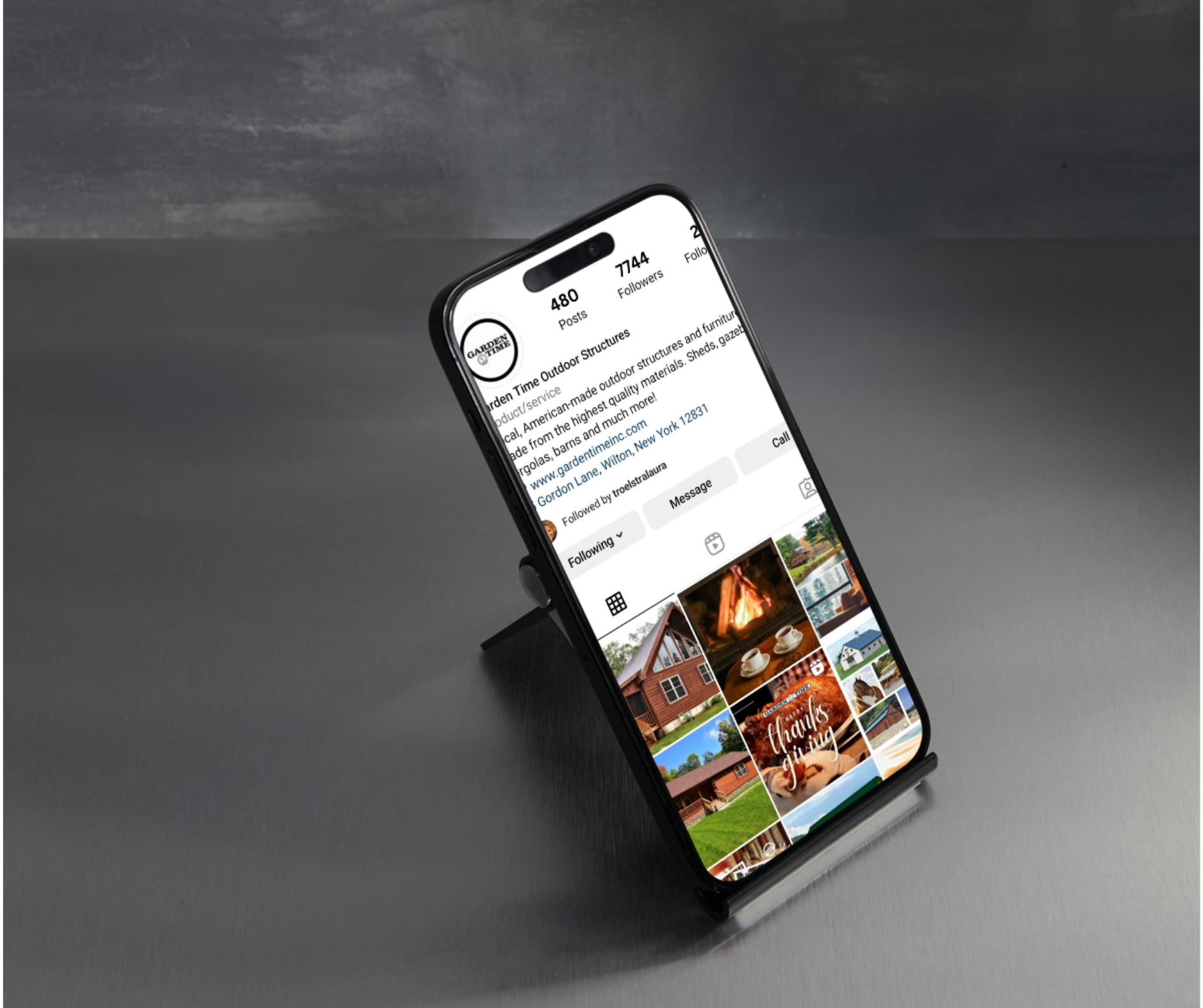 Smartphone on a matte surface displaying an Instagram profile for Garden Time Outdoor Structures with various photos of outdoor homes and decor.