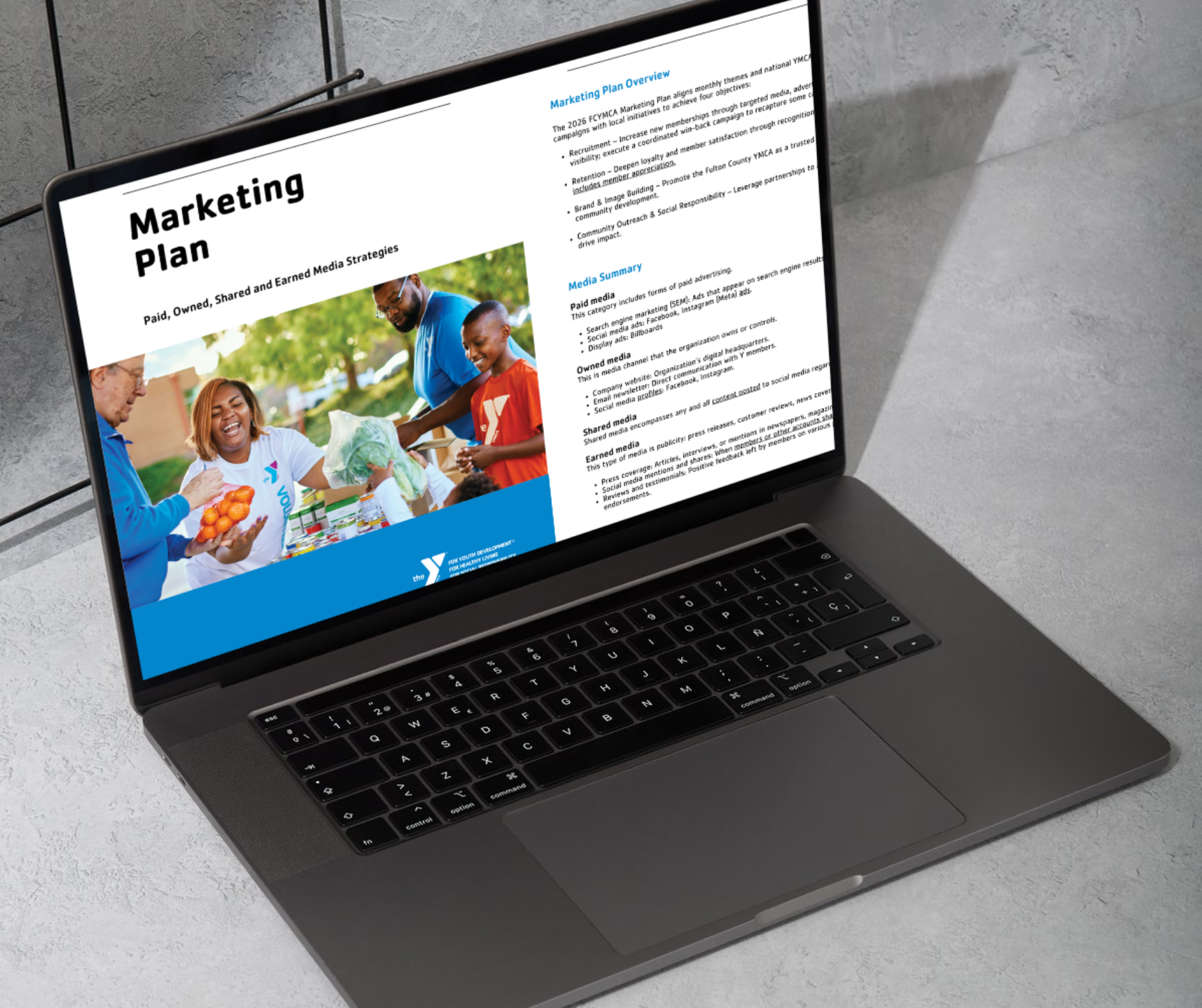 Laptop on concrete surface displaying a marketing plan for a youth development organization, featuring a photo of smiling diverse people at a community event.