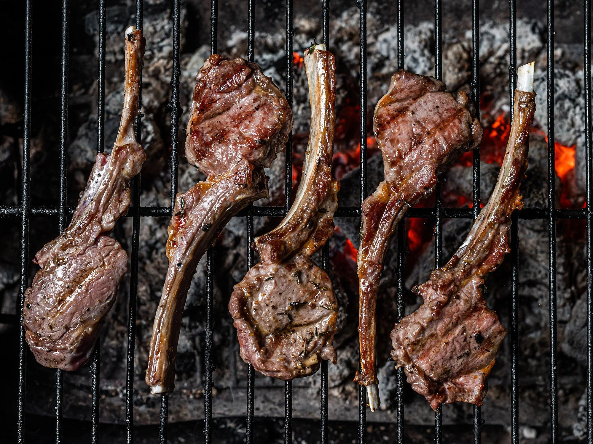 Four grilled lamb chops on a barbecue grill over hot coals.