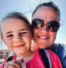 A mom and her three daughters seated in a park, enjoying quality time outdoors during a family scavenger hunt adventure