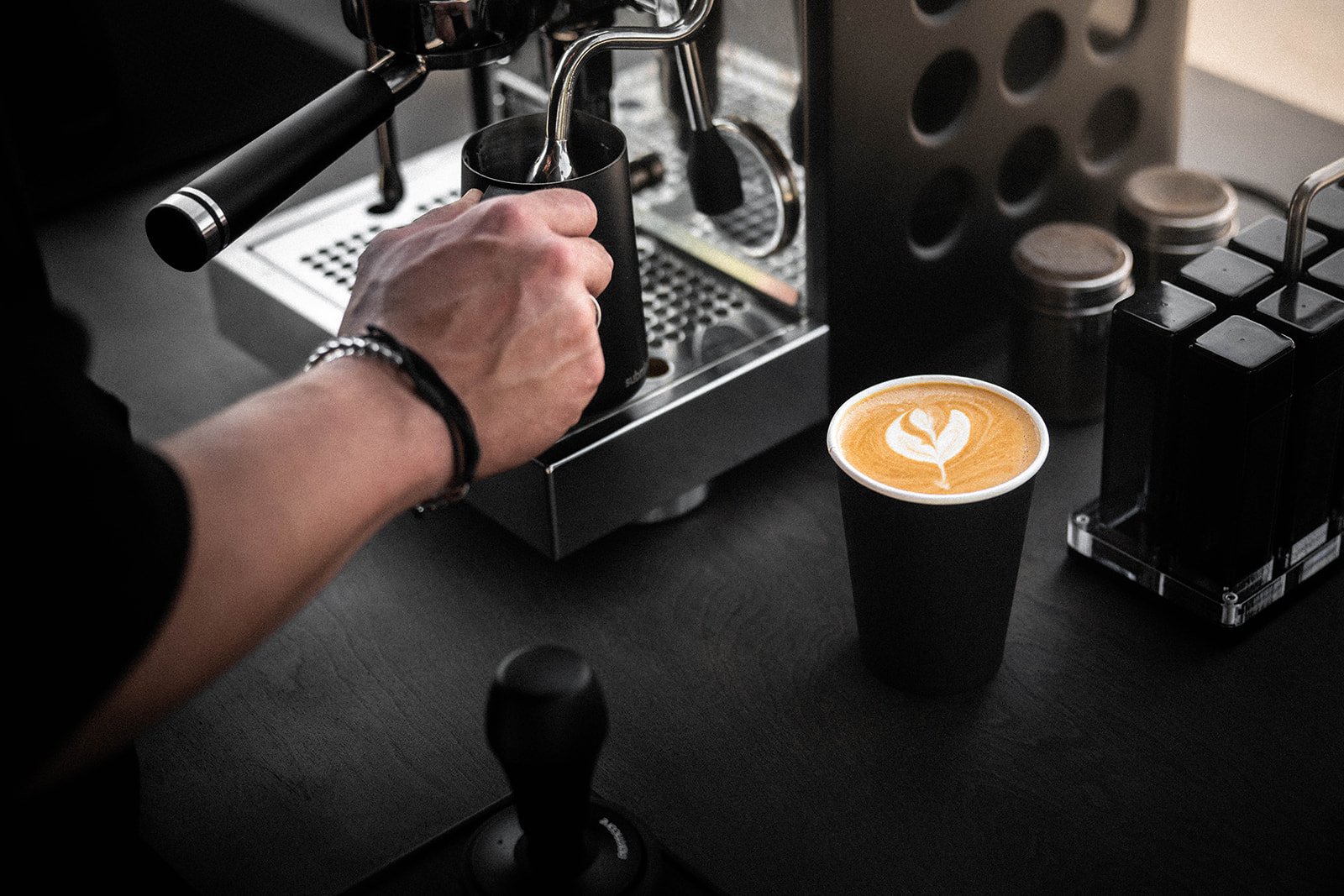 Barista using espresso machine with latte art in cup nearby on counter.