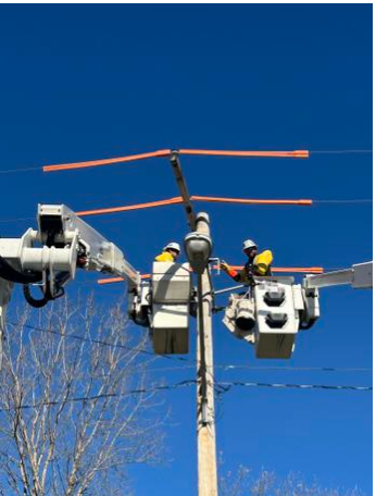 Linemen repairing an outdoor electrical utility pole with a blue sky background.