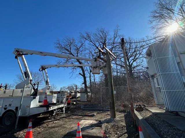 Electric utility crew repairing power lines with bucket trucks and safety cones on a sunny day.