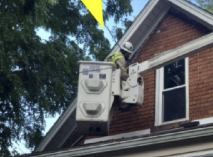 A worker in safety gear repairing or inspecting an upper window on a brick house using a bucket lift.
