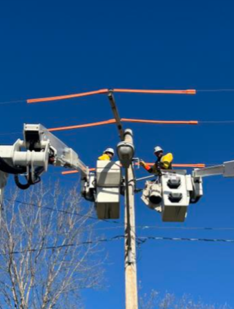 Two workers in safety gear on utility pole working on electrical lines.