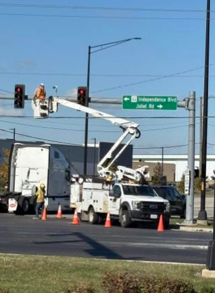 Utility workers repairing traffic signals with a bucket truck on a city street, near street signs for Independence Blvd and Juliet Rd