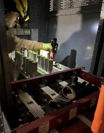 Electrician working on electrical components inside an electrical panel or control cabinet, using a screwdriver.