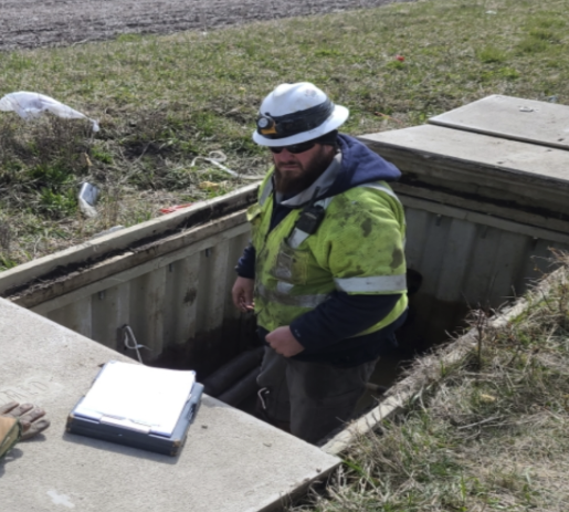 Worker in safety gear inspecting a utility hole or underground electrical box.