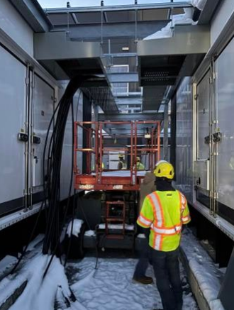 Utility workers operating equipment inside a building with snow outside, wearing safety gear and reflective vests.