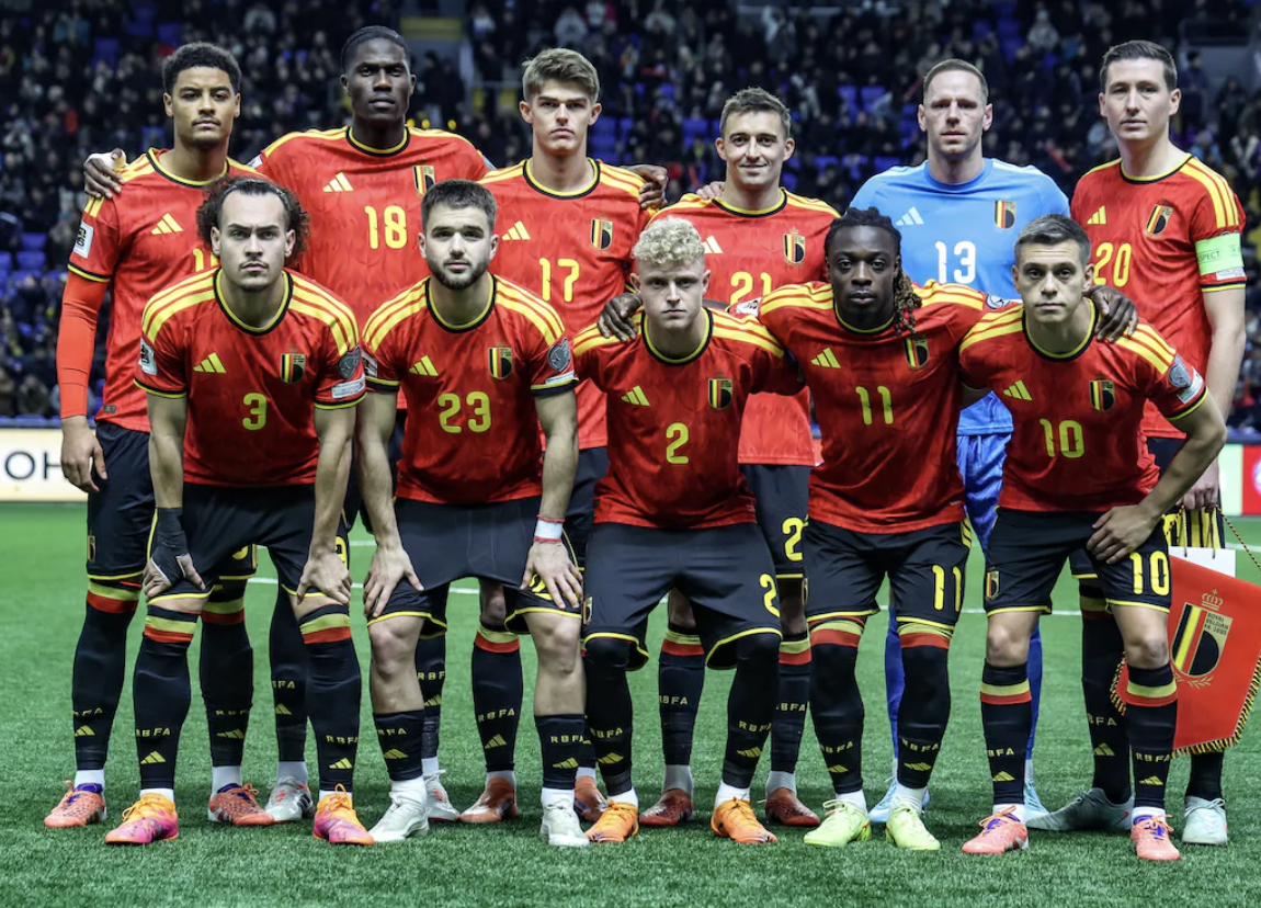 A group of eleven soccer players in red and yellow uniforms posing for a team photo on a soccer field.