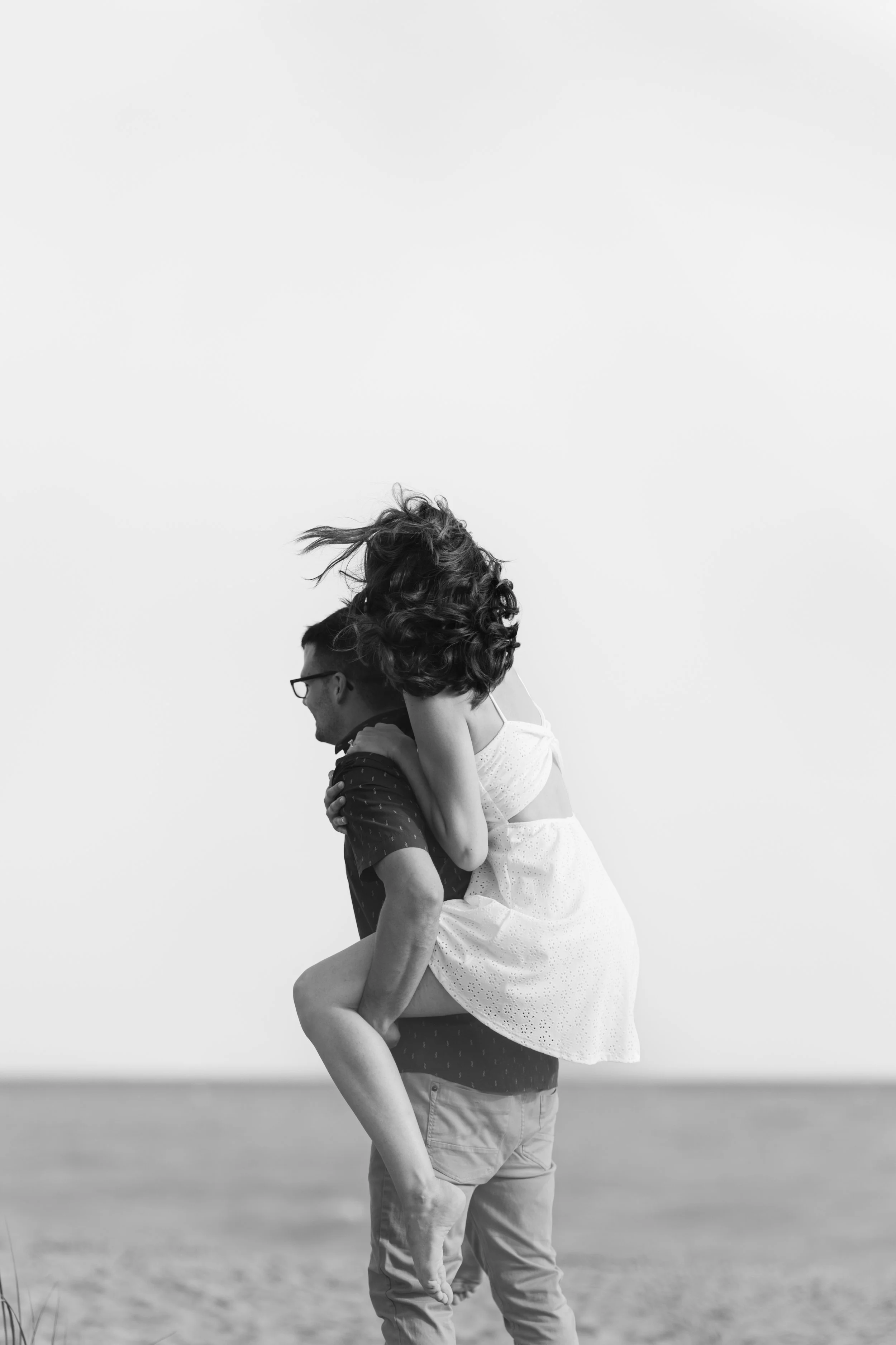 A couple on the beach, with the man carrying the woman on his shoulders. They are in black and white.