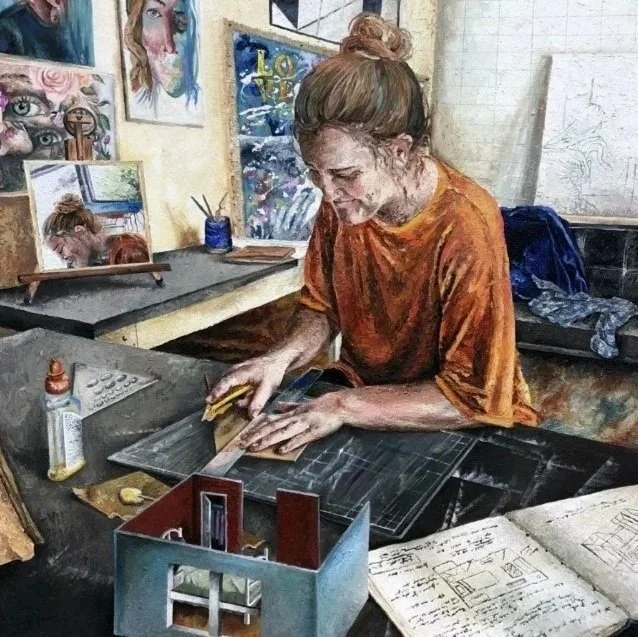 An artist with red hair tied up, wearing an orange shirt, working at a desk in an art studio. She is using a cutter tool on a framed piece of art. The studio has paintings on the wall, including a portrait of a woman and colorful artwork. Various art supplies and sketches are visible on the desk.