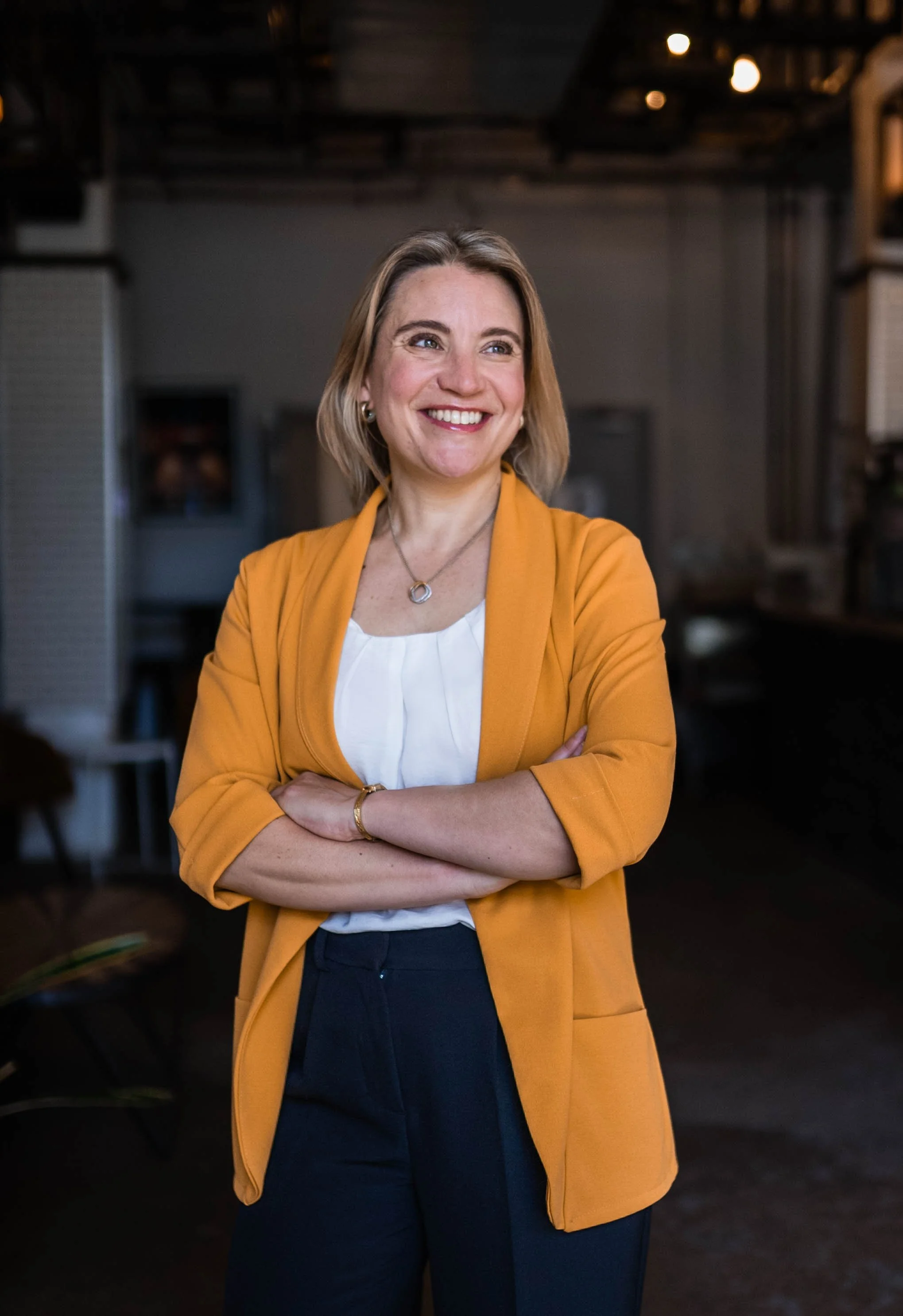 Woman with short blonde hair wearing yellow cardigan smiles into the distance
