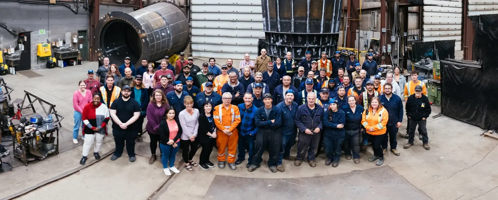 A large group of people posing inside a factory or warehouse with industrial equipment around them.