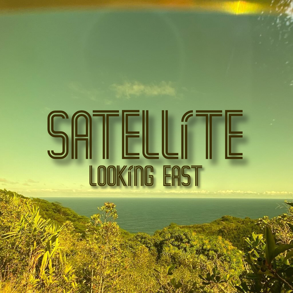 A photograph through a green lens of the ocean and lush foliage on Maui HI. The text 'Satellite' and 'Looking' East is in the center of the frame. A lens flare type effect near the top of frame.