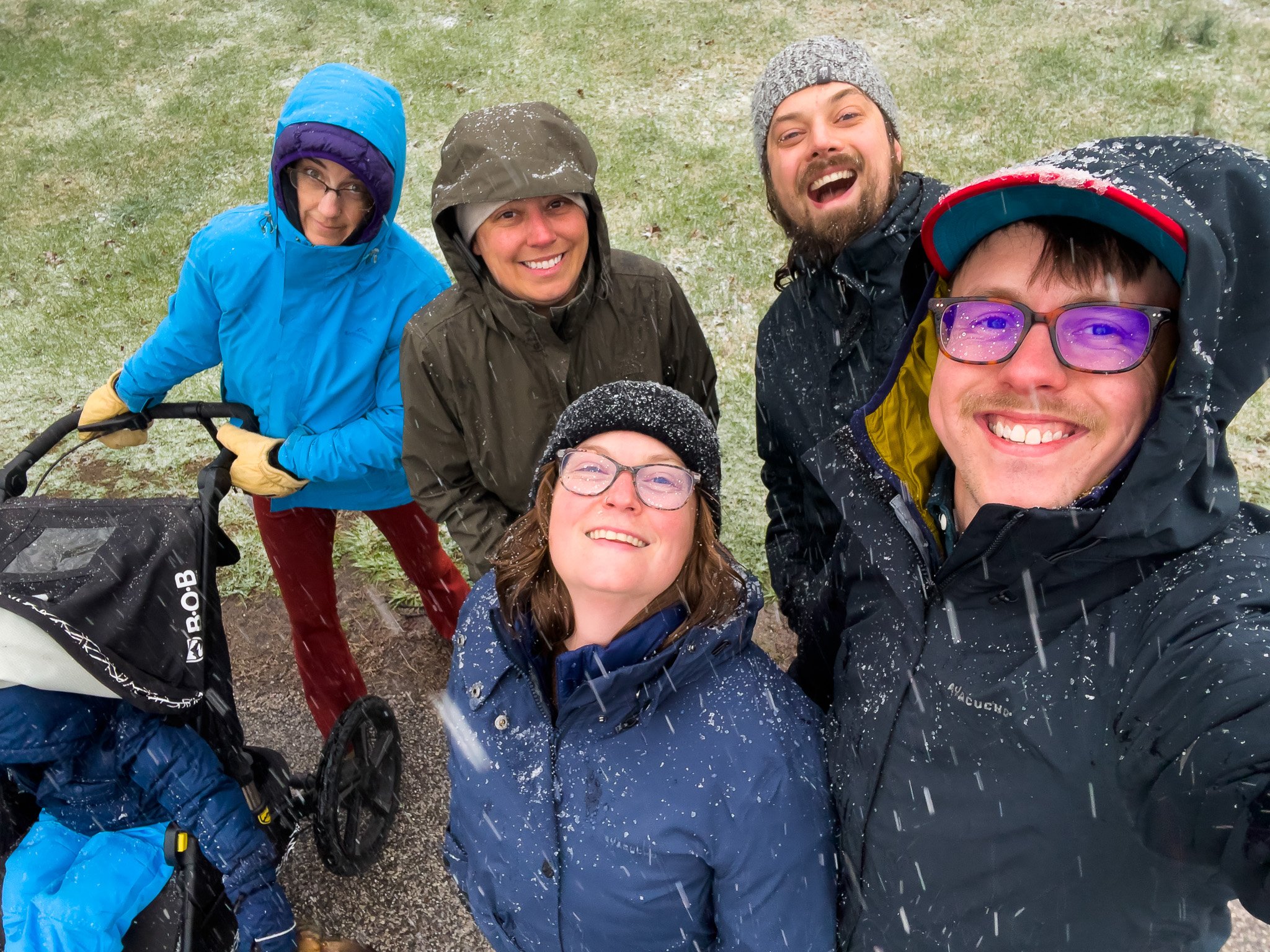 Group of six people outside on a snowy day, smiling and taking a selfie.