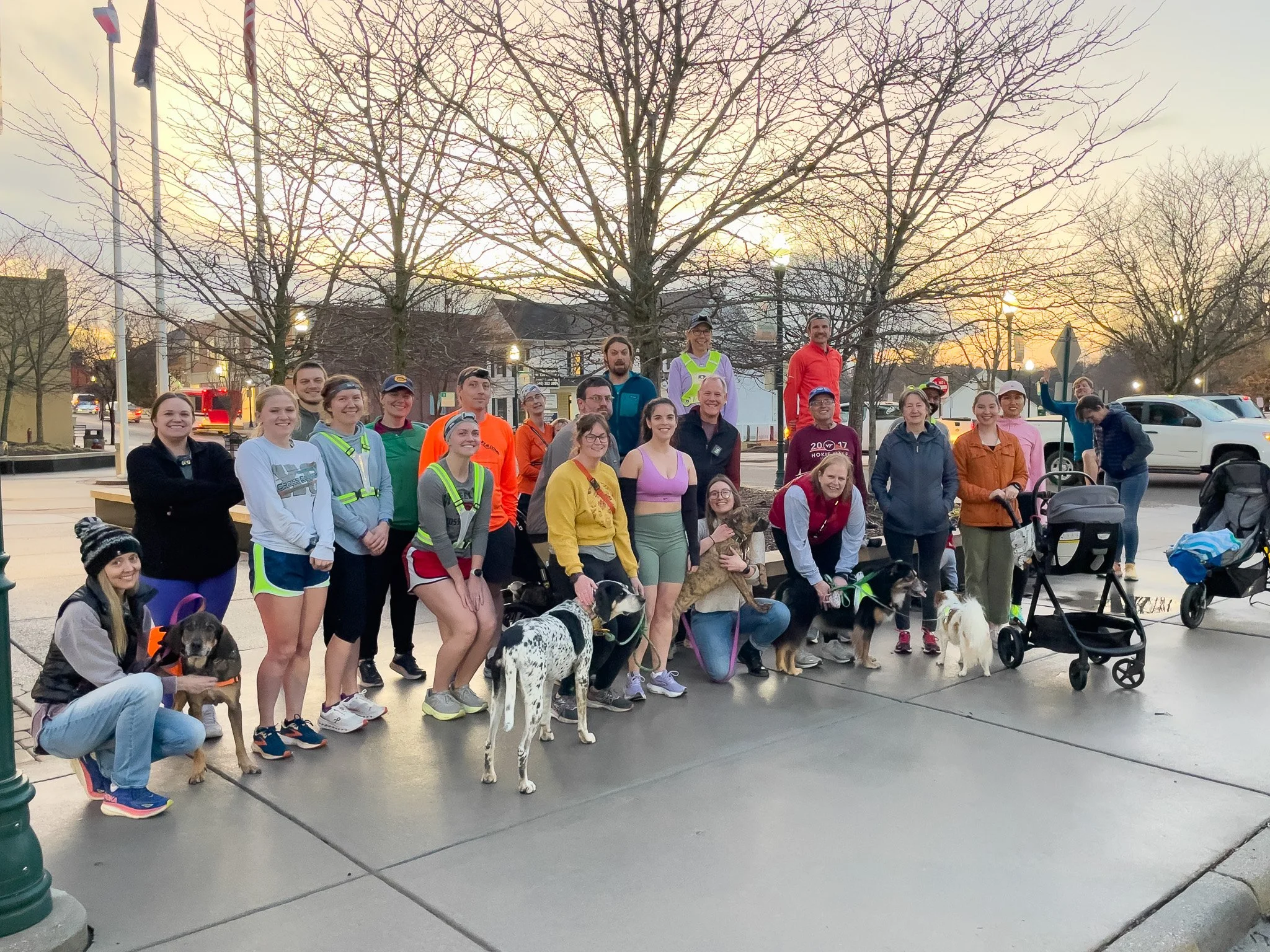 Group of people gathered outdoors during sunset, some holding or with service dogs, participating in a community event or walk.