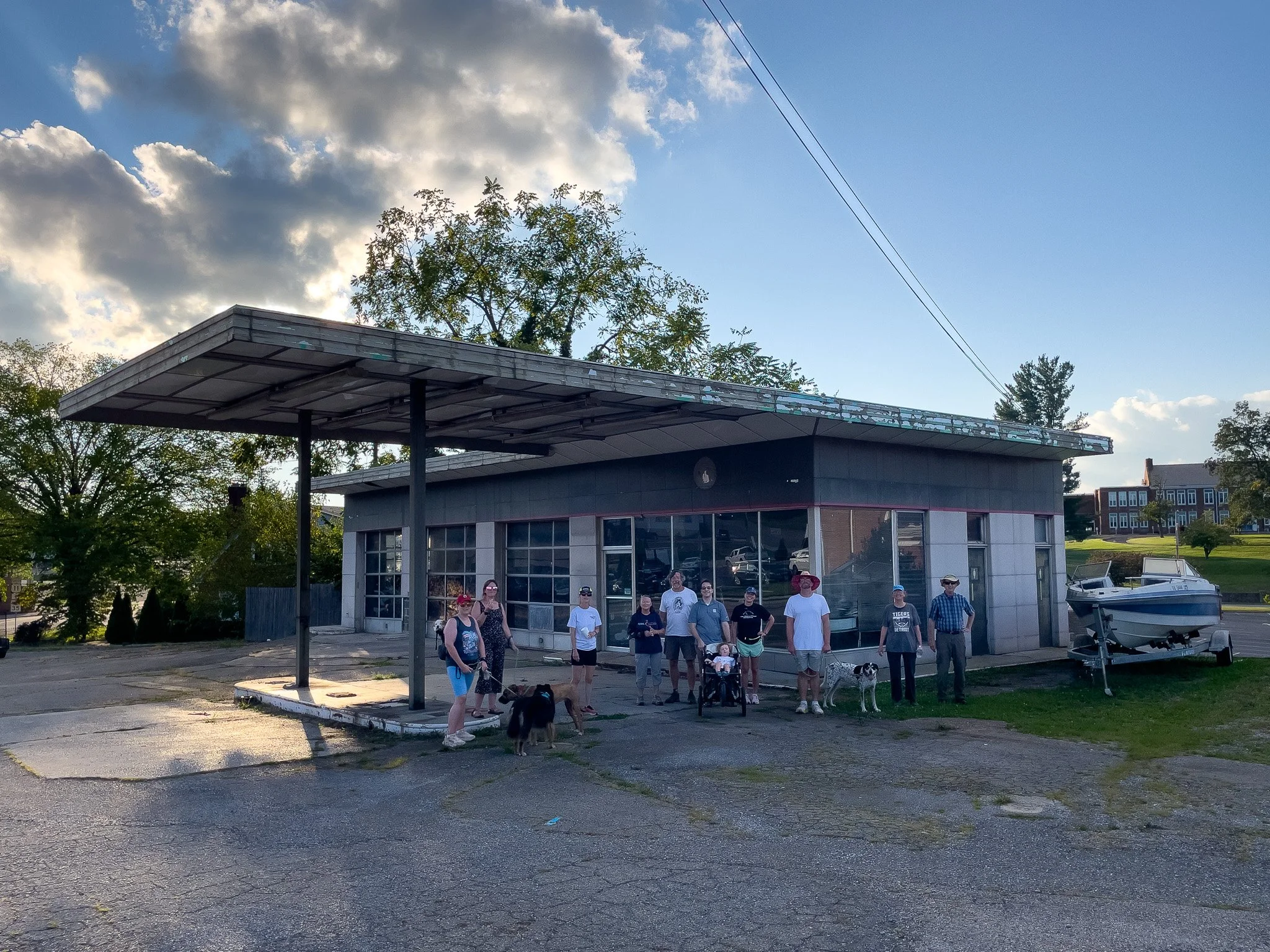 Group of people with dogs standing outside a small building with a large awning on a sunny day