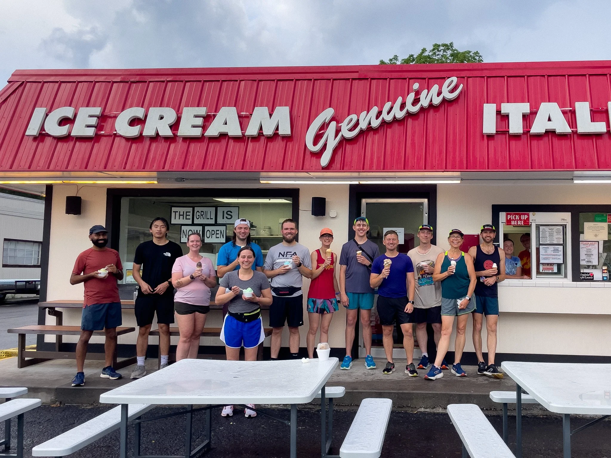 Group of people standing outside a pink ice cream shop, holding ice cream cones and smiling.