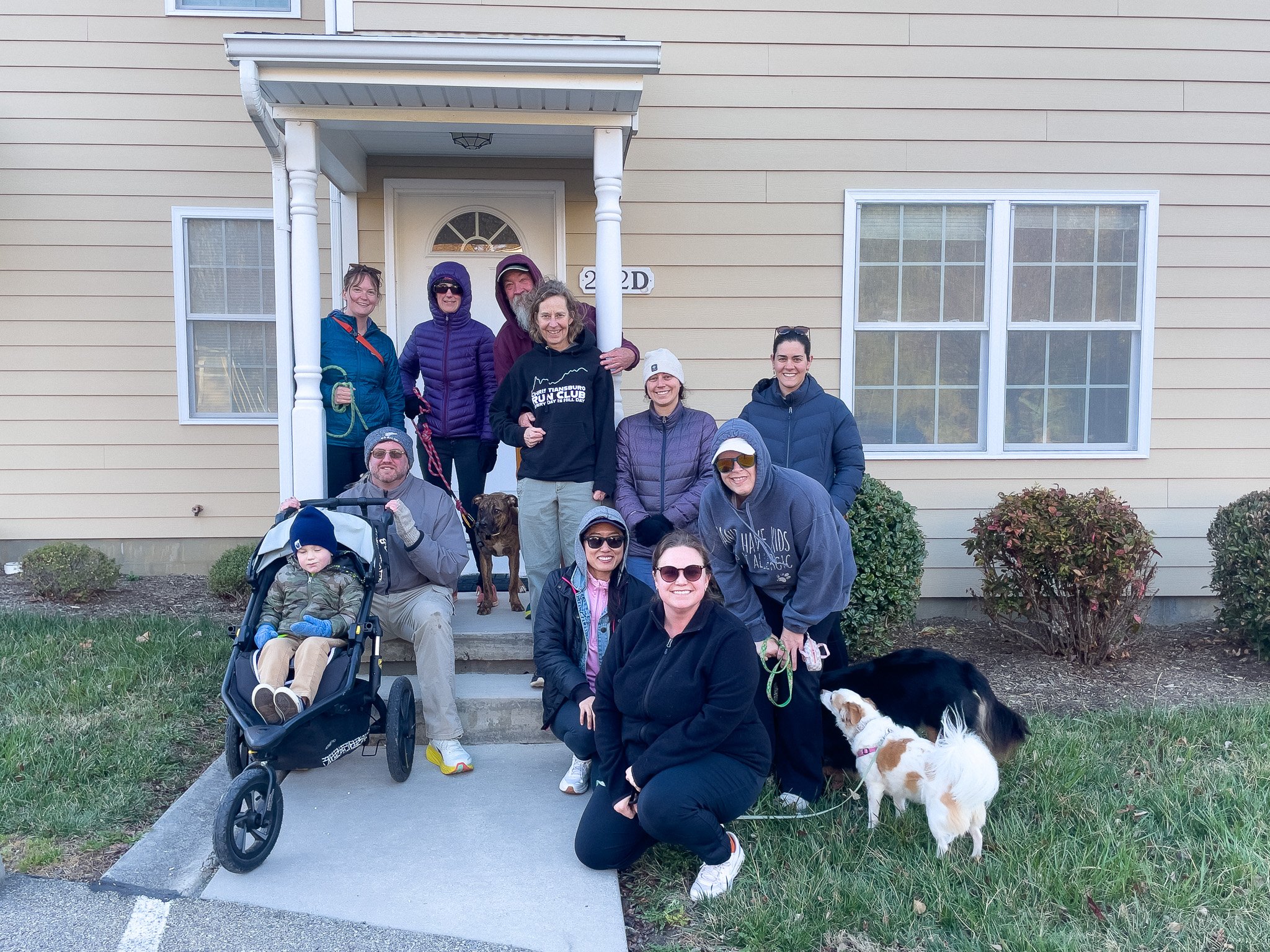 Group of people with dogs and a child on a porch in front of a house.