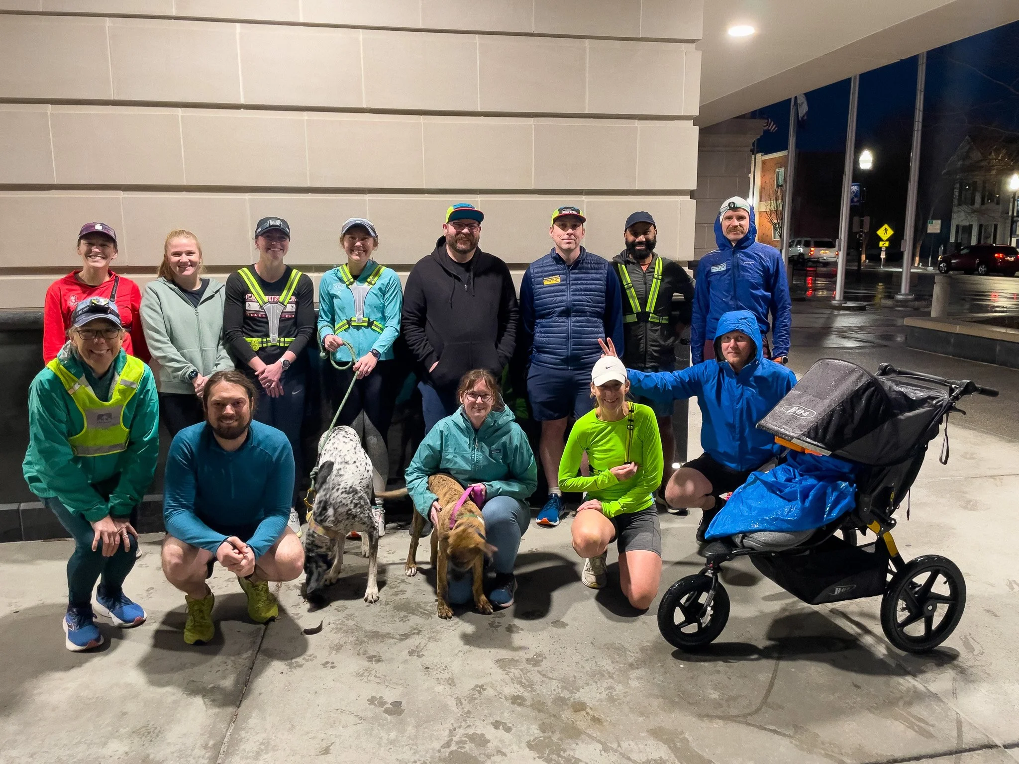 Group of people, some with dogs and a stroller, standing outside at night.