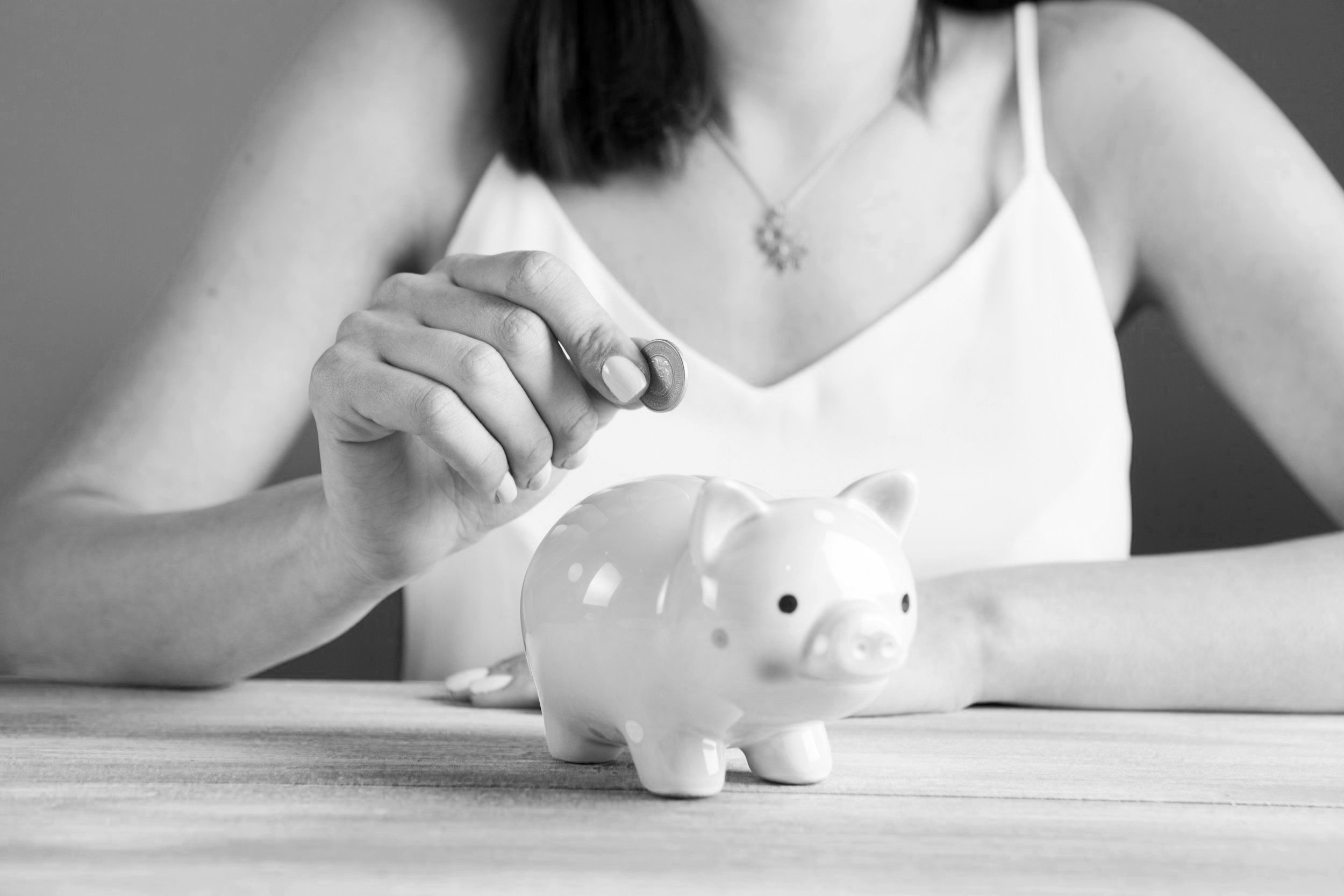 Person inserting coin into ceramic piggy bank.