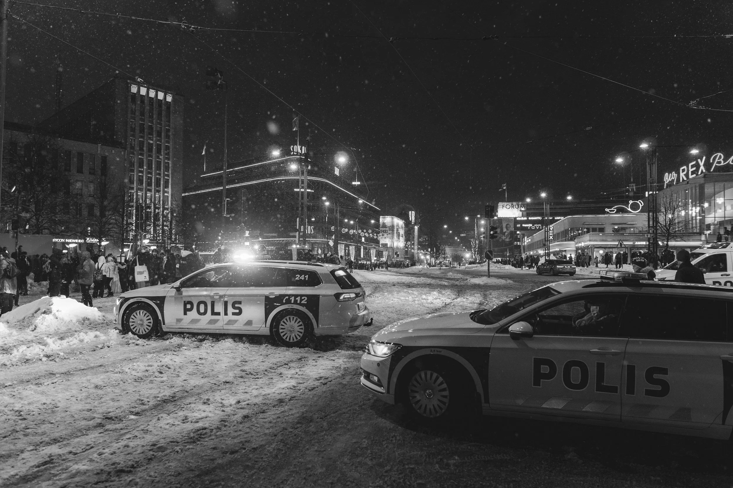 Night street scene with police cars, snow, and people.