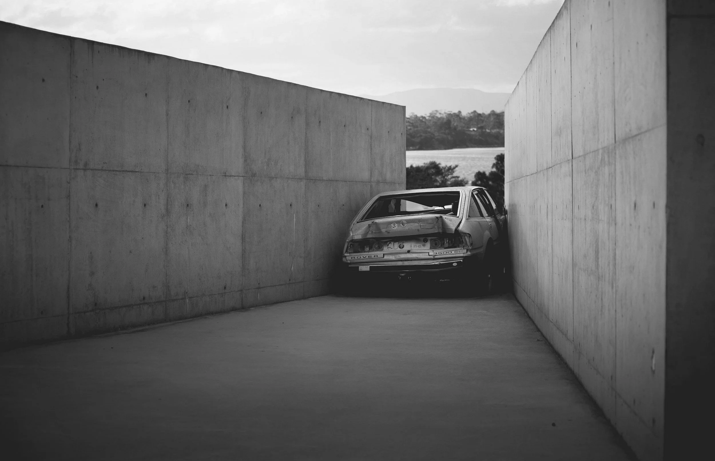 Abandoned car in narrow concrete alley, black and white photo