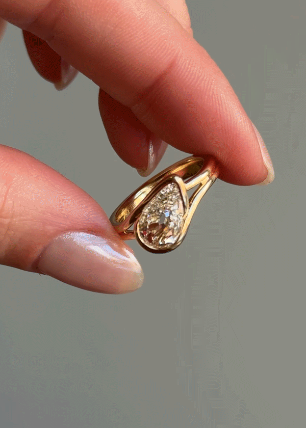 Close-up of a hand holding a gold ring with a teardrop-shaped diamond and smaller diamonds inside the teardrop.