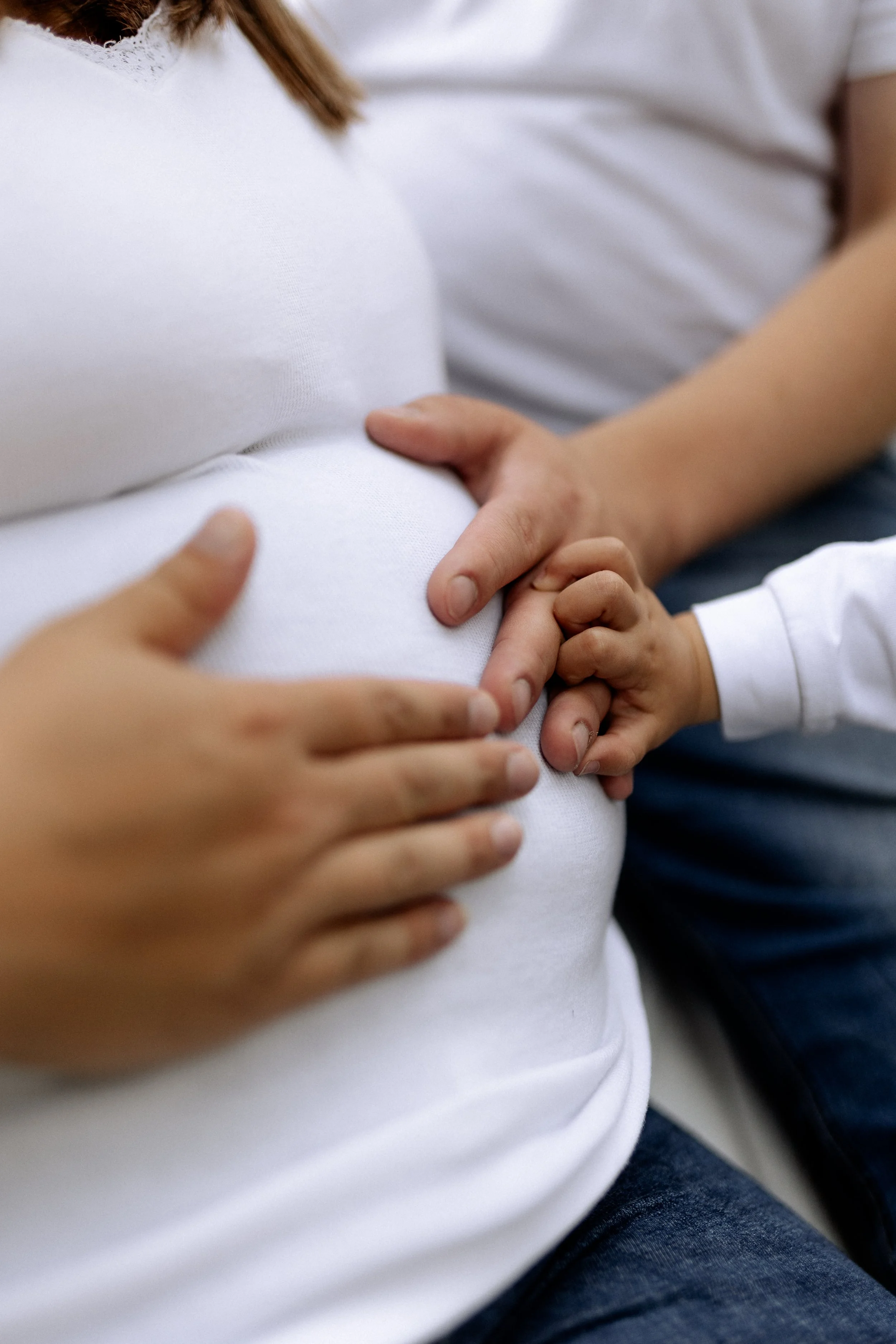 Eine schwangere Frau mit einem Babyfinger, der ruhig auf ihrem Bauch liegt, und einer Hand, die den Bauch hält.